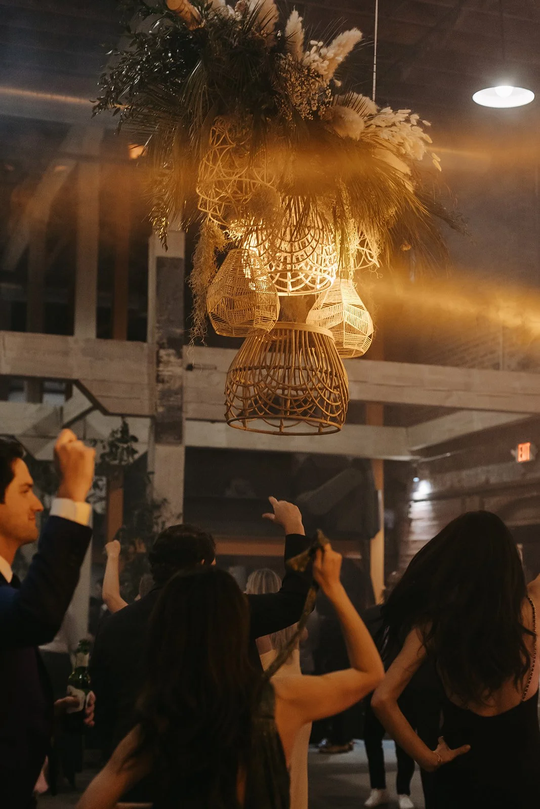 People dancing and socializing at a party with warm lighting and decorative wicker lamps hanging from the ceiling.