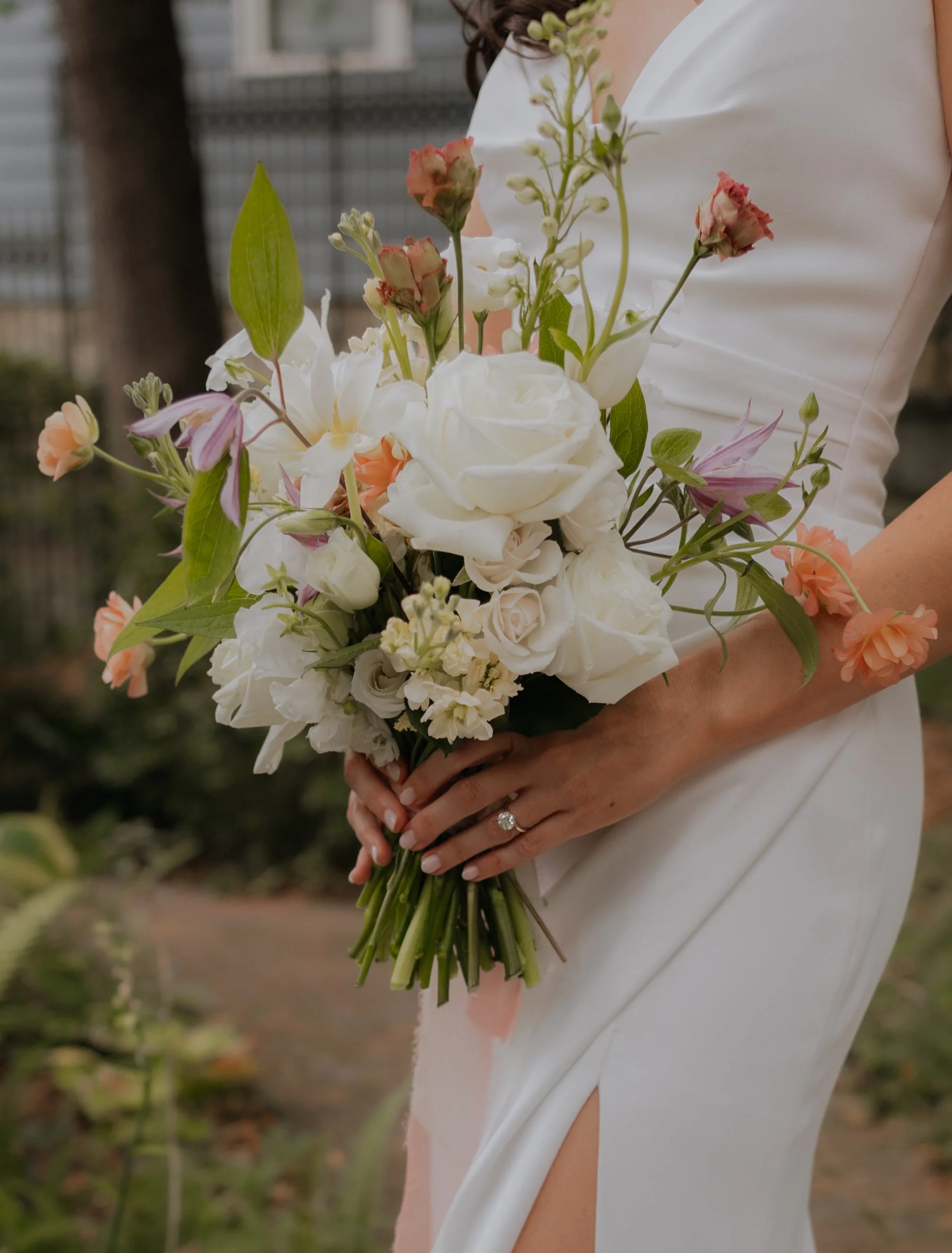 A woman in a white dress holding a bouquet of white and pink flowers with green leaves.
