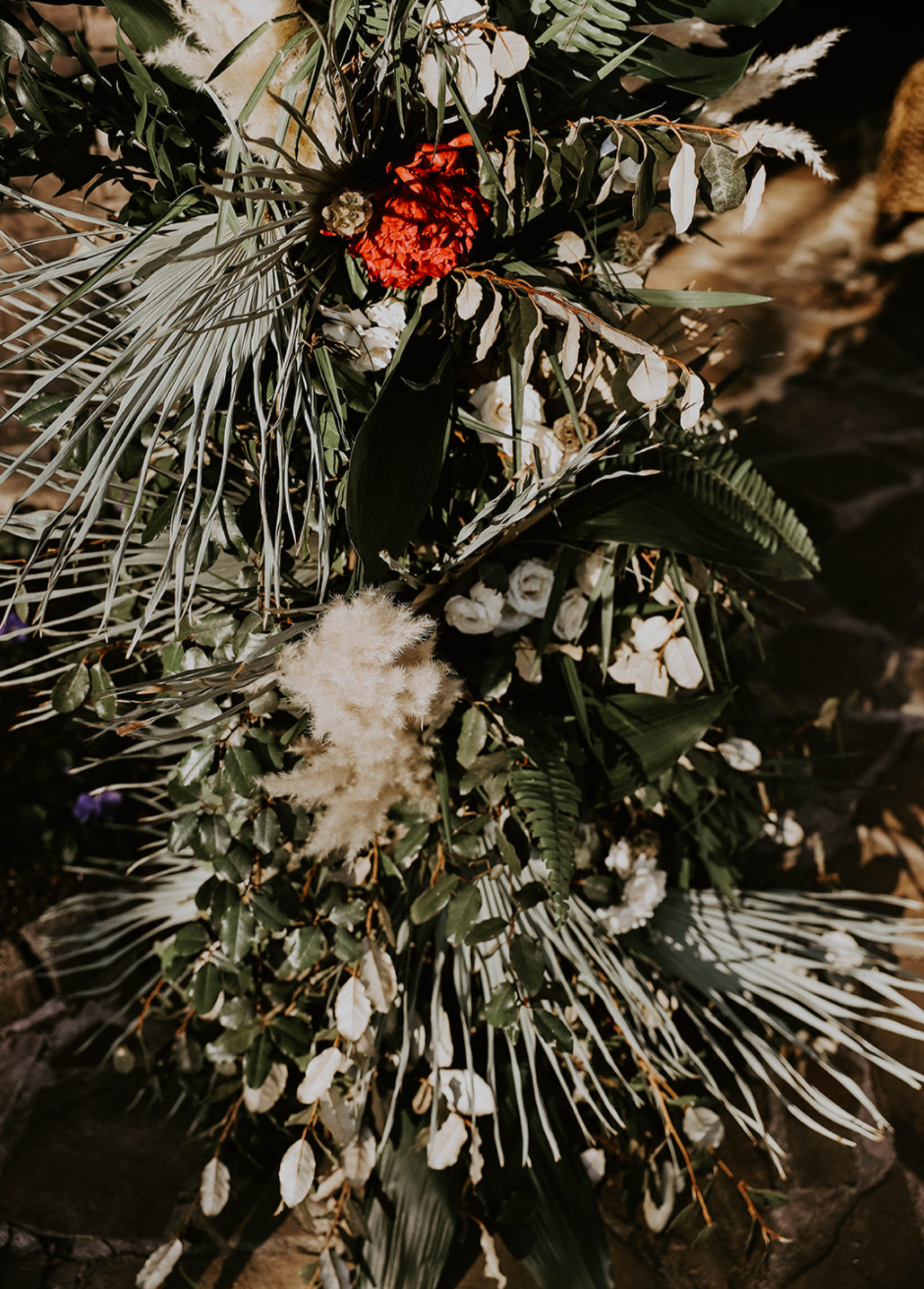Arrangement of various flowers and greenery, including a prominent red flower, white flowers, and different types of leaves.