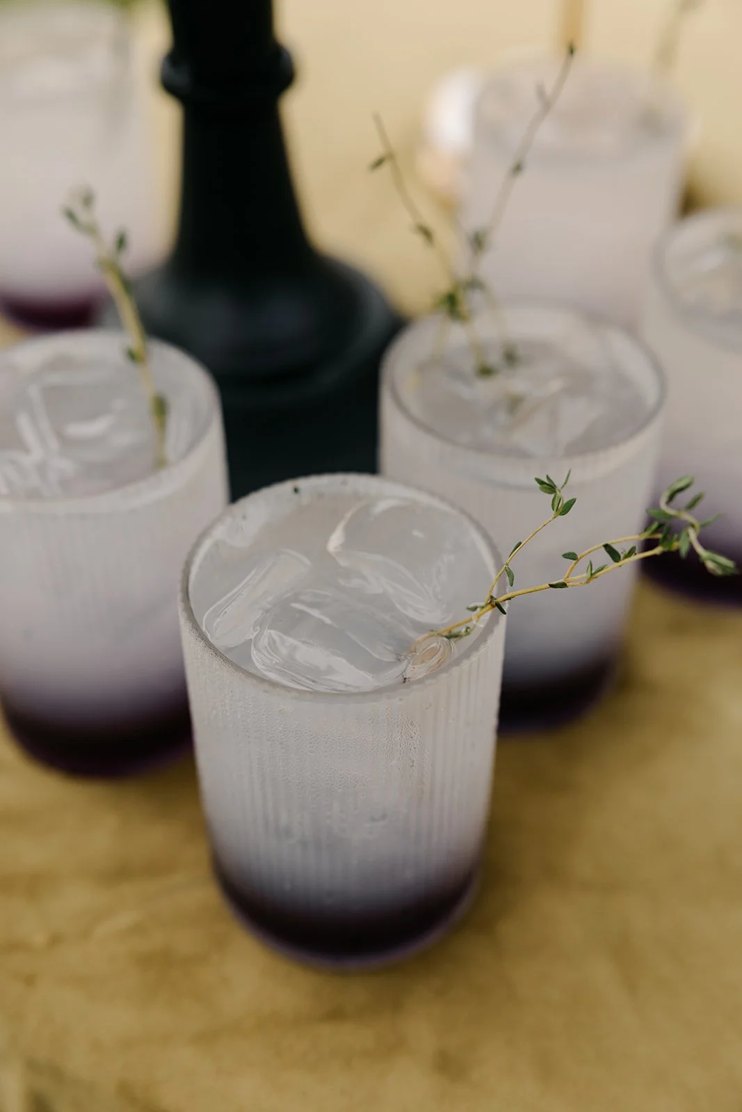 Clear drinks with ice and sprigs of herbs in tall, textured glasses
