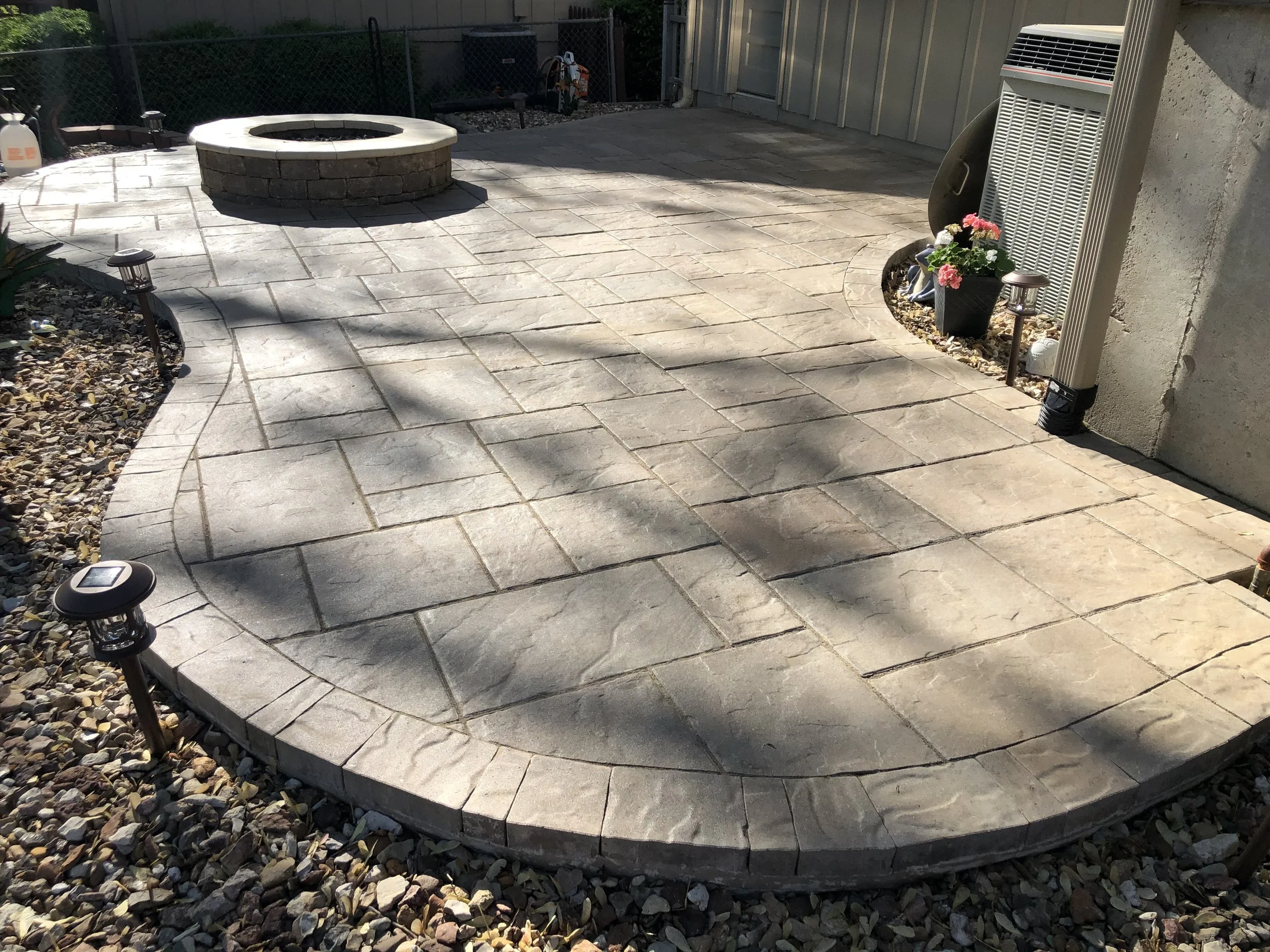 Flower pots, outdoor lanterns, and a fire pit on a paved patio area of a backyard.