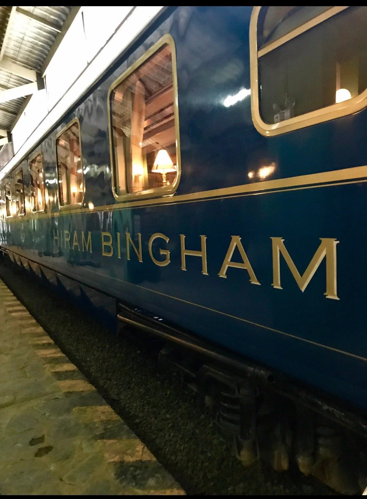 A vintage blue train car with gold lettering that reads "GIRAM BINGHAM." The train is inside a station with a stone platform and a metal roof, and warm interior lighting is visible through the windows.