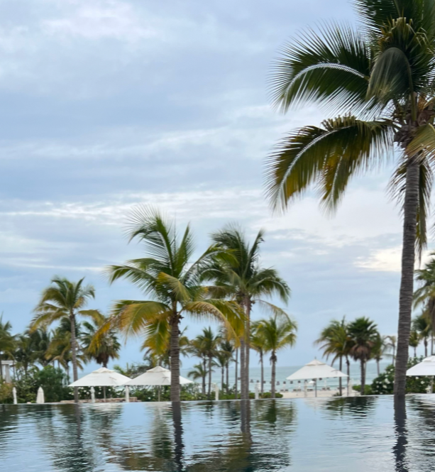 Pool with palm trees and white umbrellas under a cloudy sky