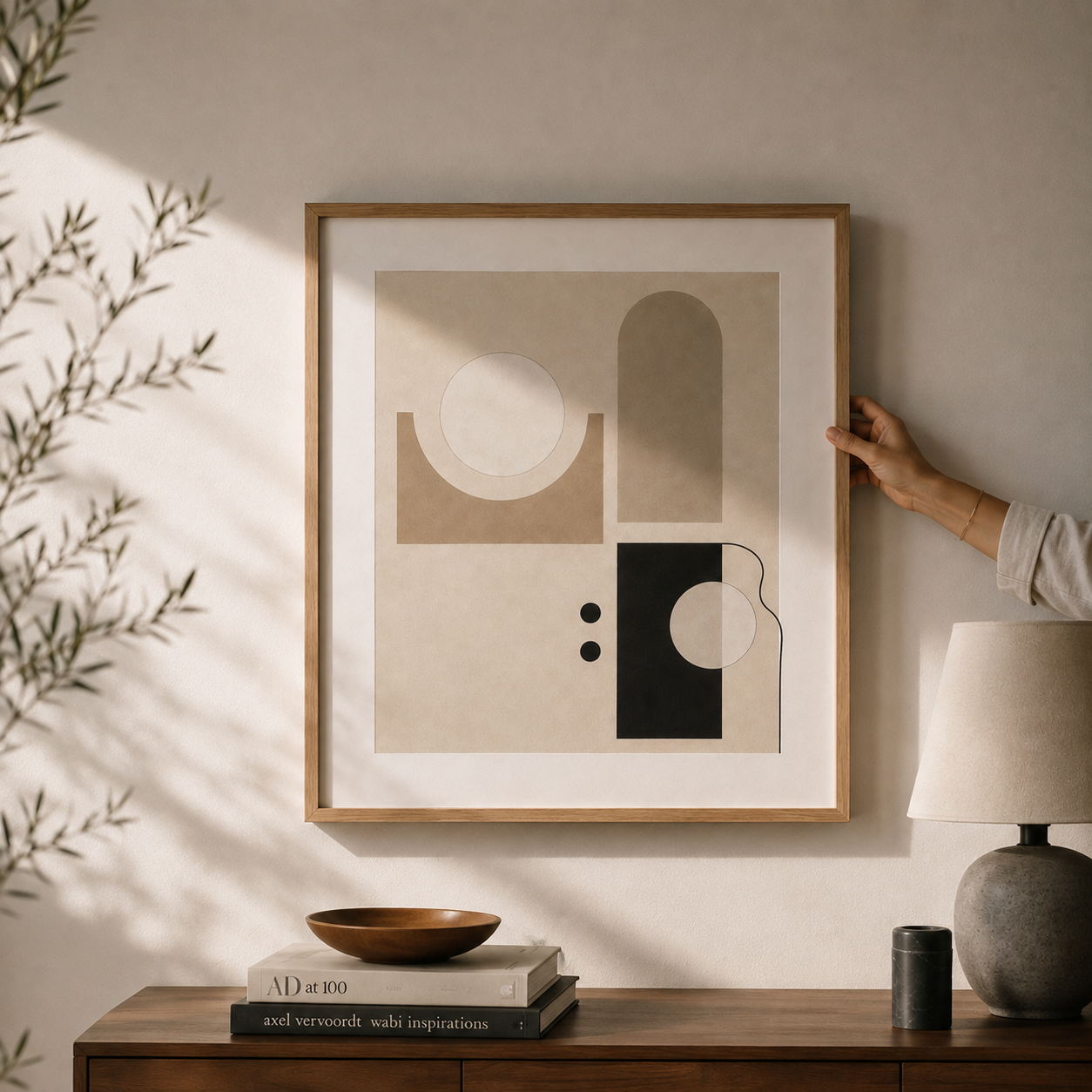 Framed abstract wall art being carefully positioned in a California modern residential interior with warm morning light, minimalist styling, and natural oak frame.
