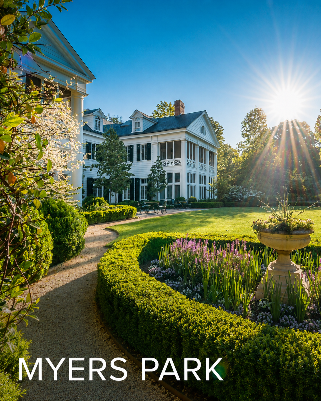 A grand white house with a large wraparound porch, surrounded by well-manicured gardens and lush greenery under a clear blue sky with the sun shining brightly.