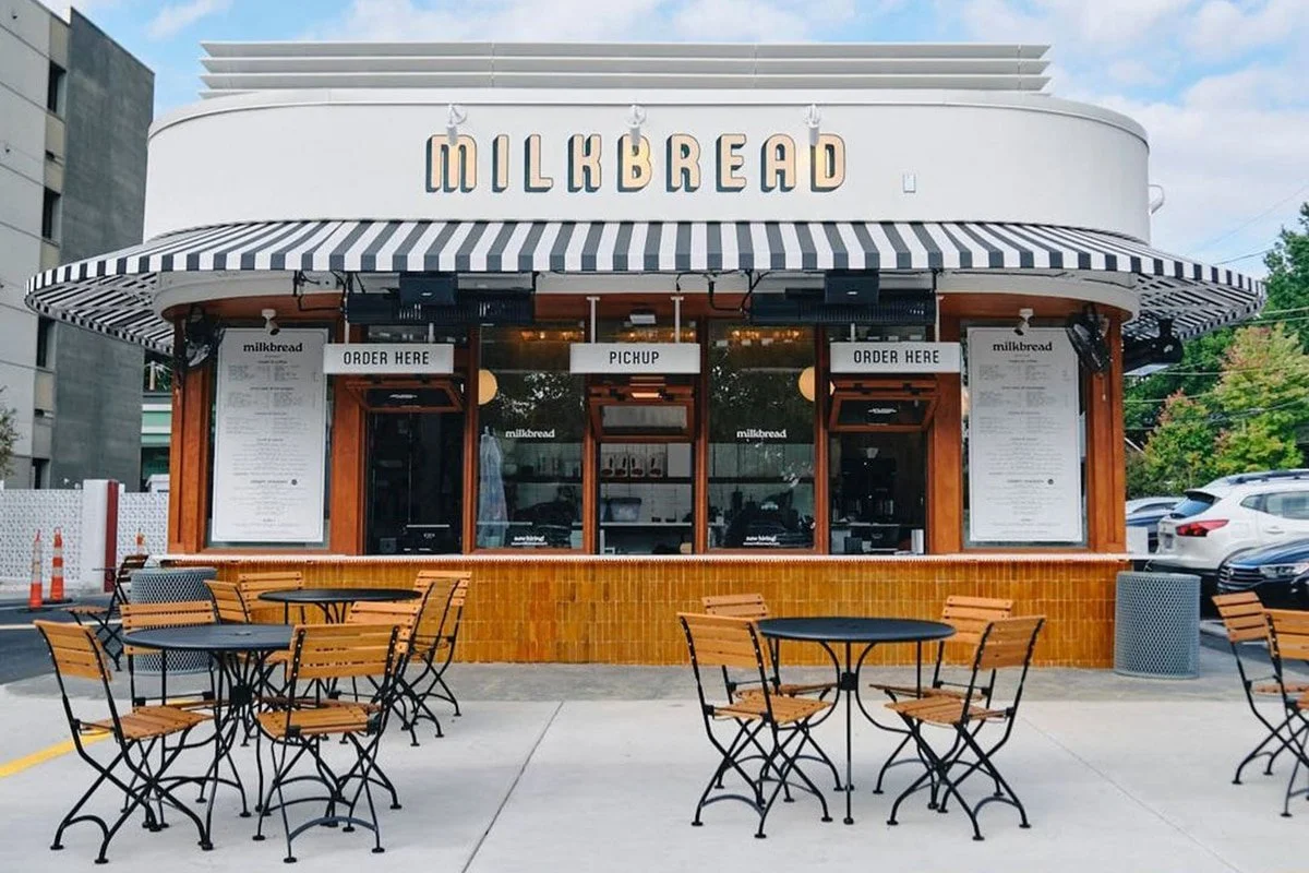 Exterior of a Milkbread bakery with outdoor seating and a striped awning, with signs for ordering and pickup.