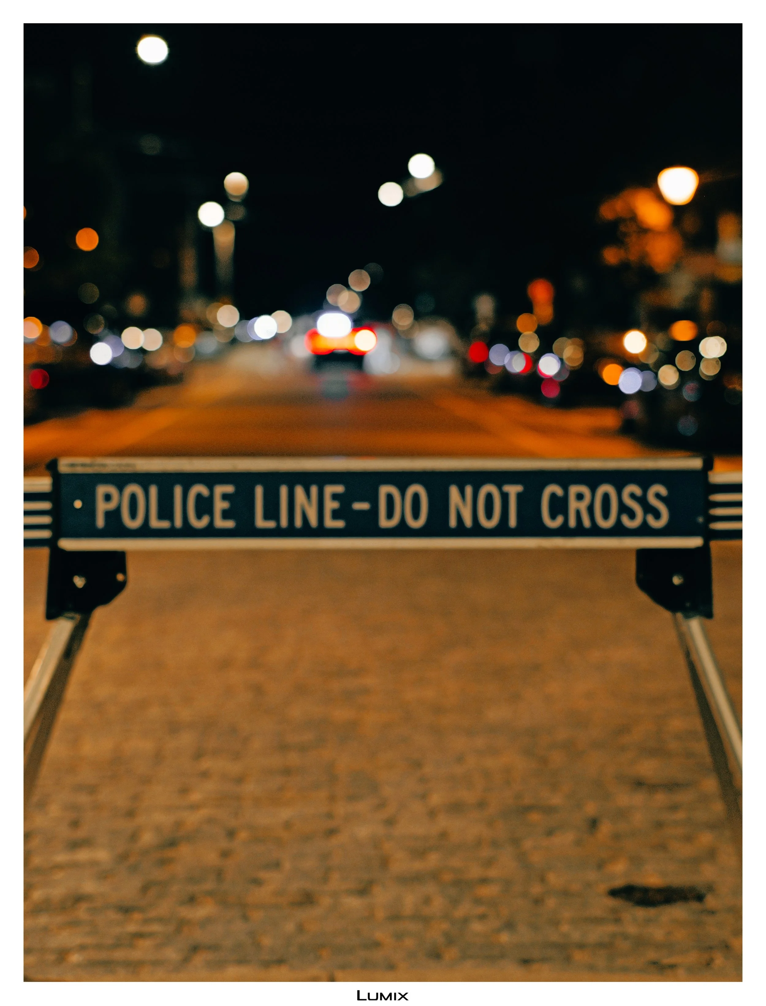 Blurred night view of a city street with streetlights and car lights, with a police line do not cross barrier in the foreground.