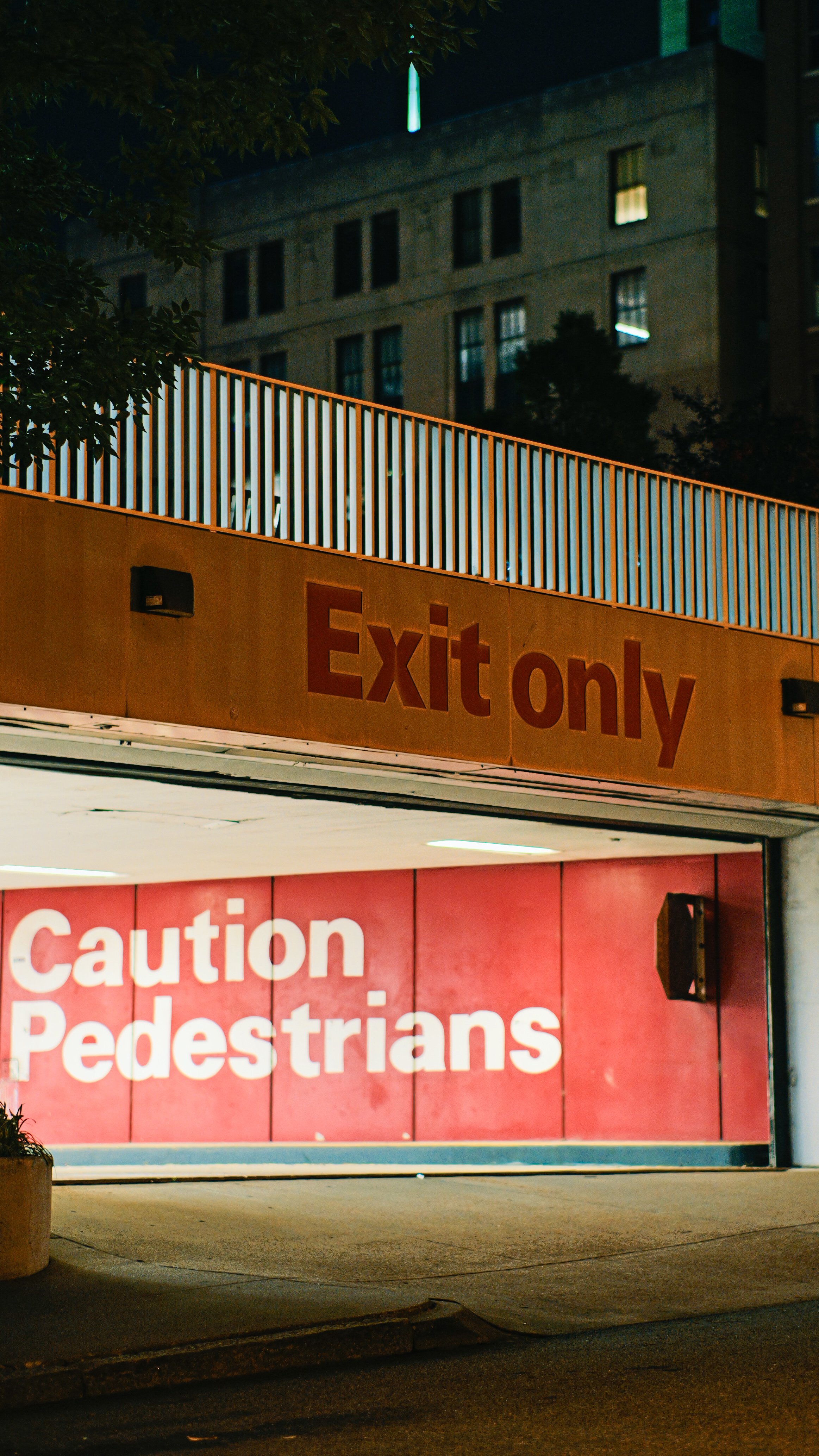 A parking garage entrance with a large red sign warning of pedestrians, with an orange sign above reading 'Exit only'.