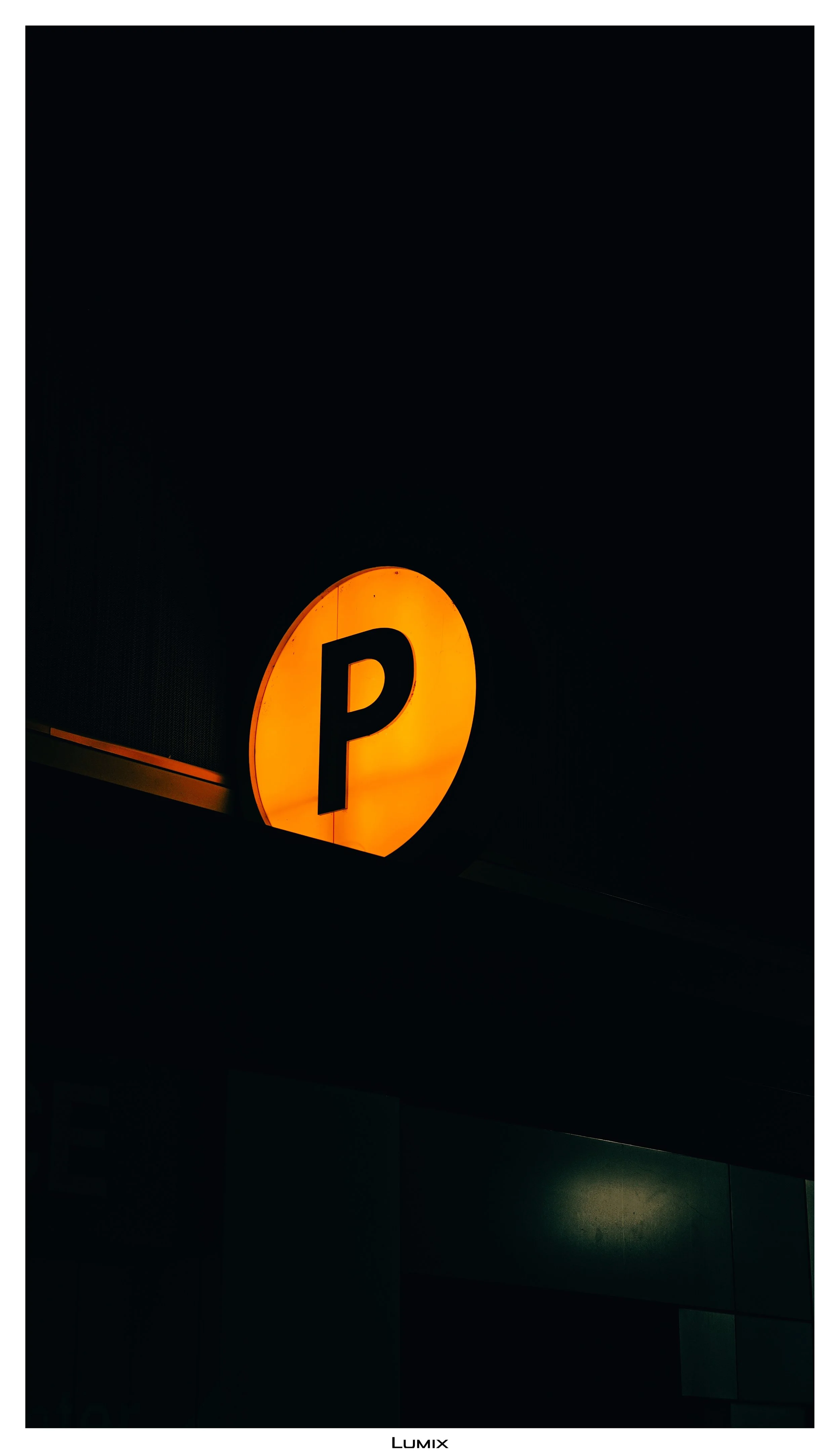 Illuminated orange parking sign with a black letter 'P' on a dark building exterior at night.