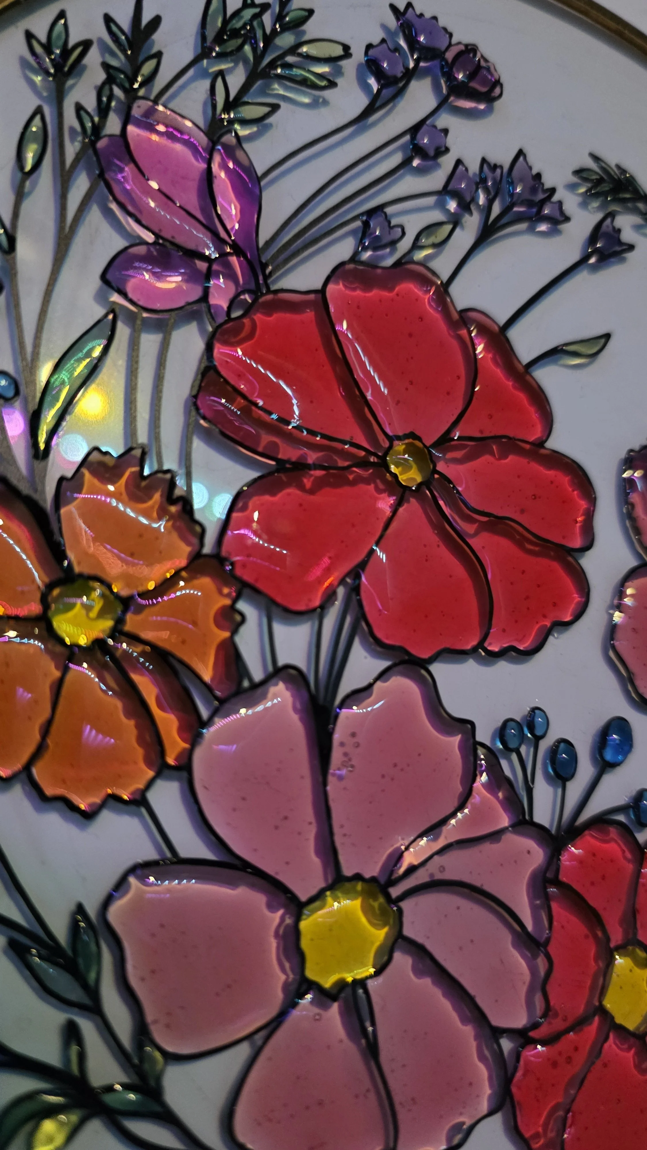 Colorful stained glass artwork of flowers with pink, purple, orange, and yellow petals and green leaves.