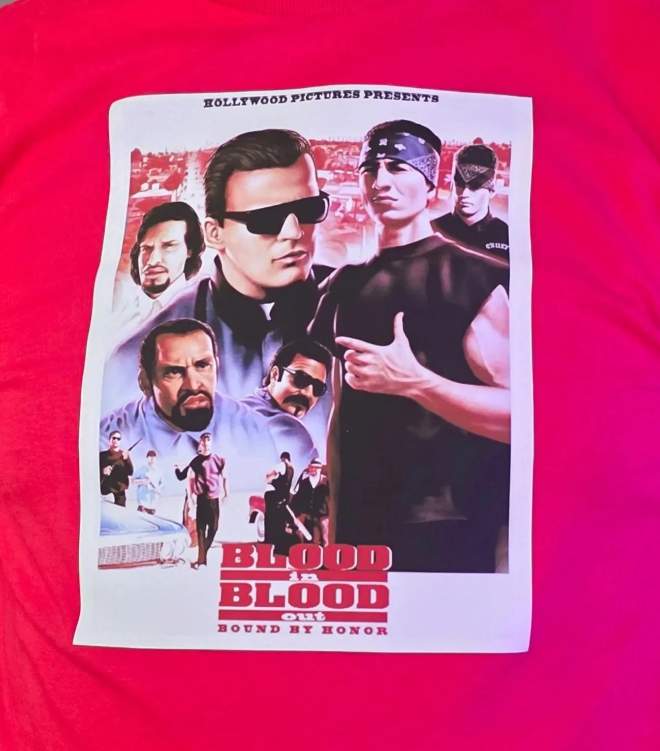 A person wearing a red T-shirt with a graphic print of characters from the film "Blood in Blood Out".