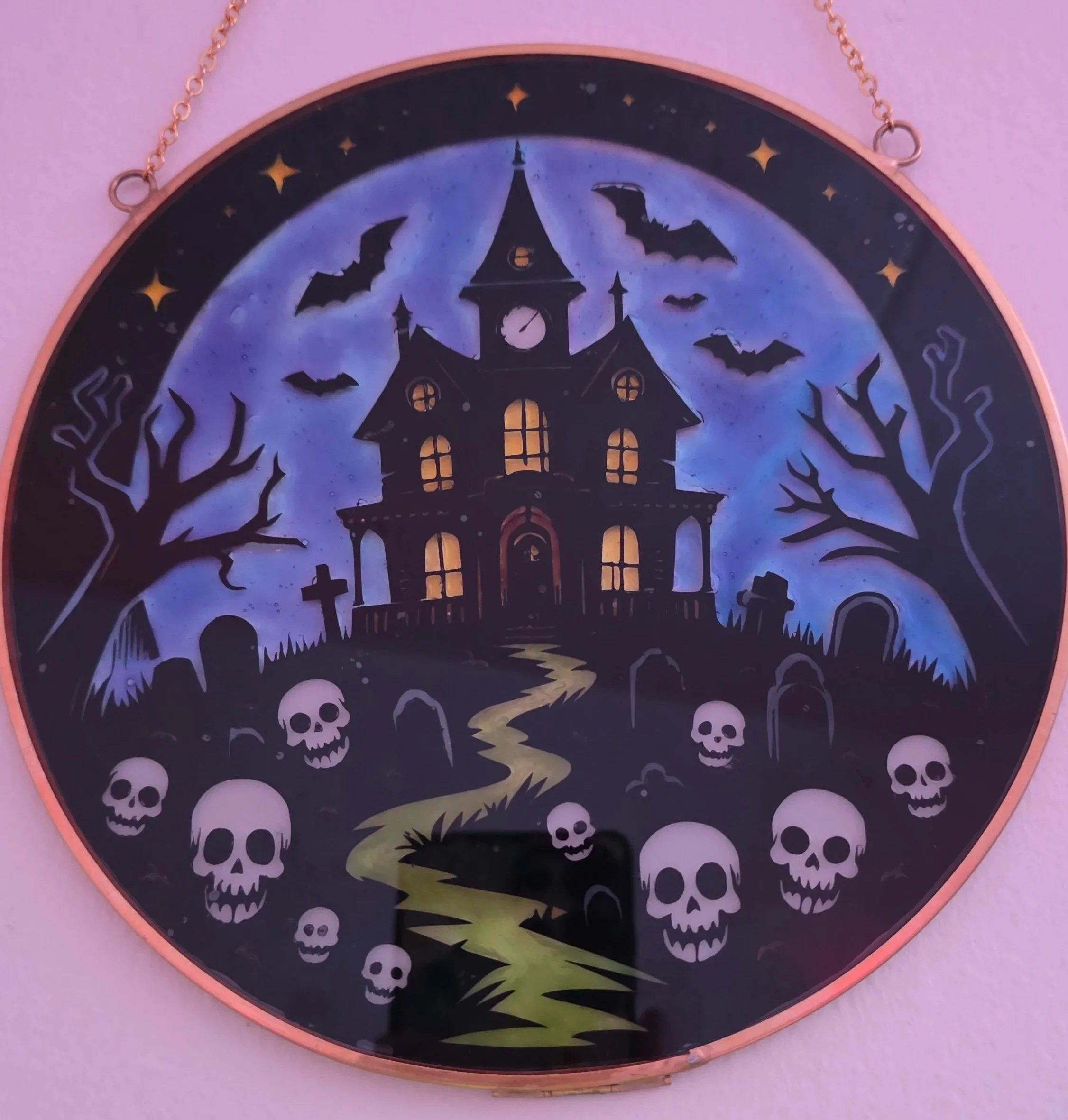 A spooky Halloween-themed clock with a haunted house, bats, skulls, leafless trees, and a winding path against a dark night sky.