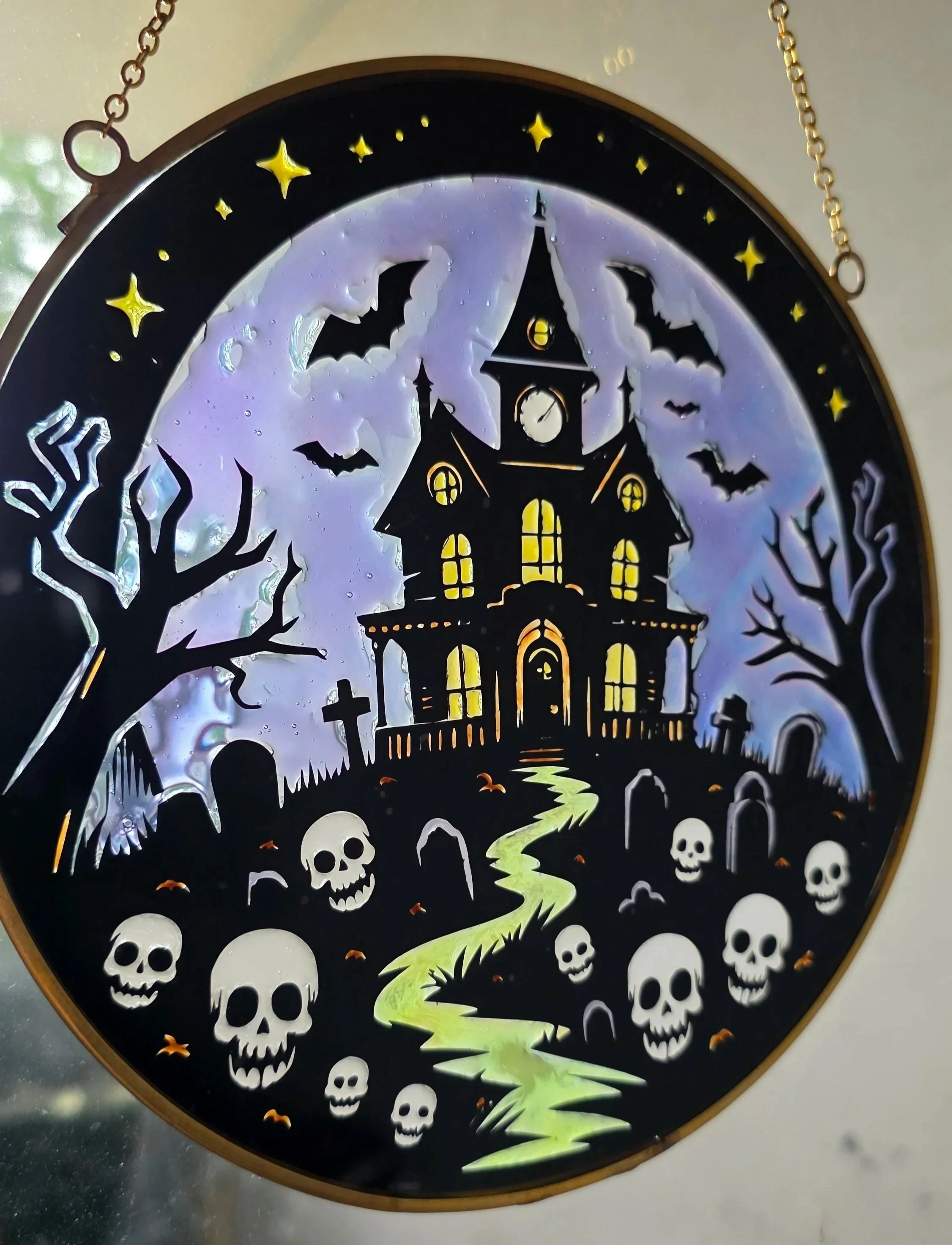 A decorative Halloween-themed clock featuring a haunted house, leafless trees, bats, skulls, a moon, and stars with glow-in-the-dark elements.