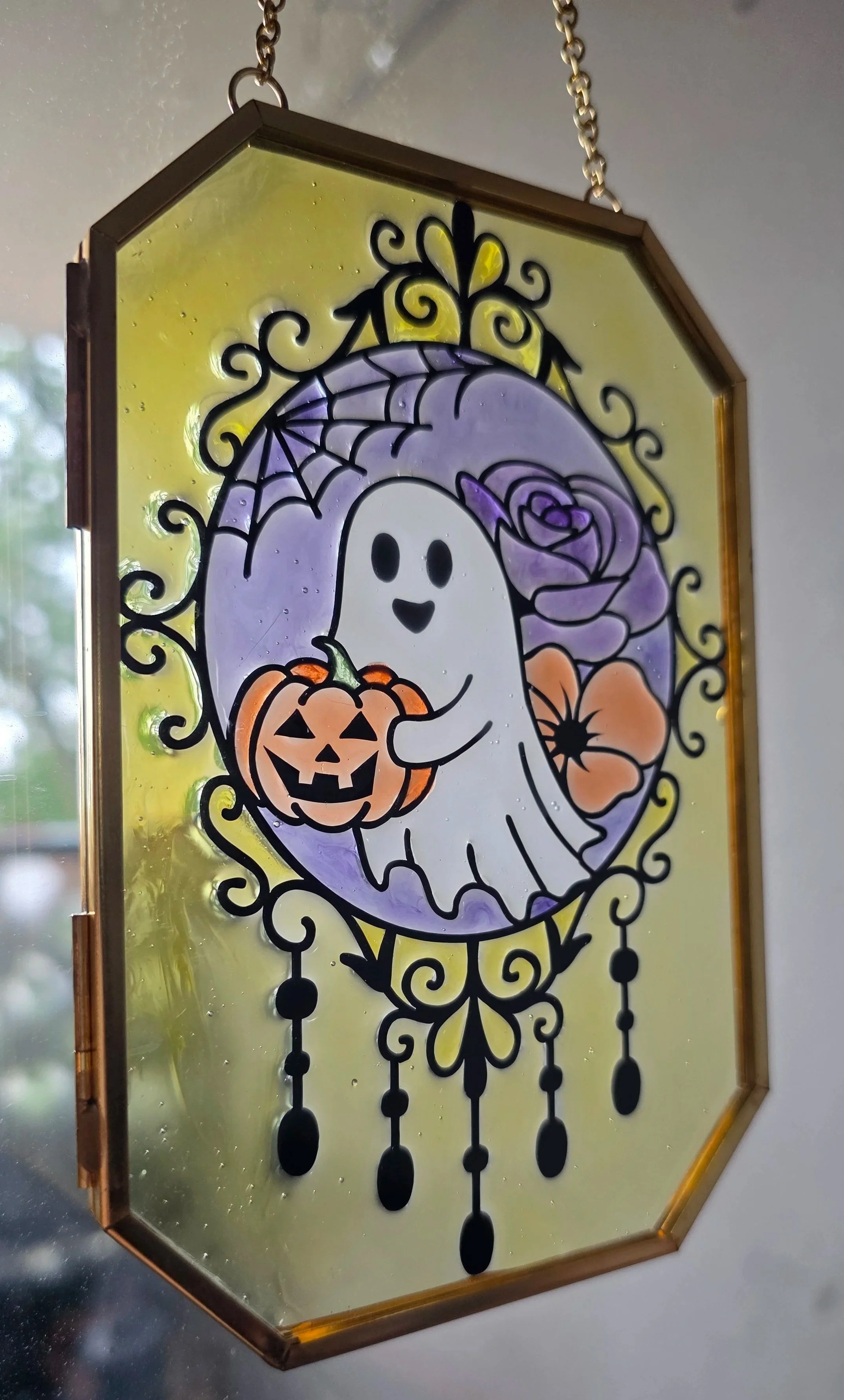 Decorative stained glass Halloween hanging panel featuring a cute ghost holding a jack-o'-lantern, purple flowers, and swirling black accents.