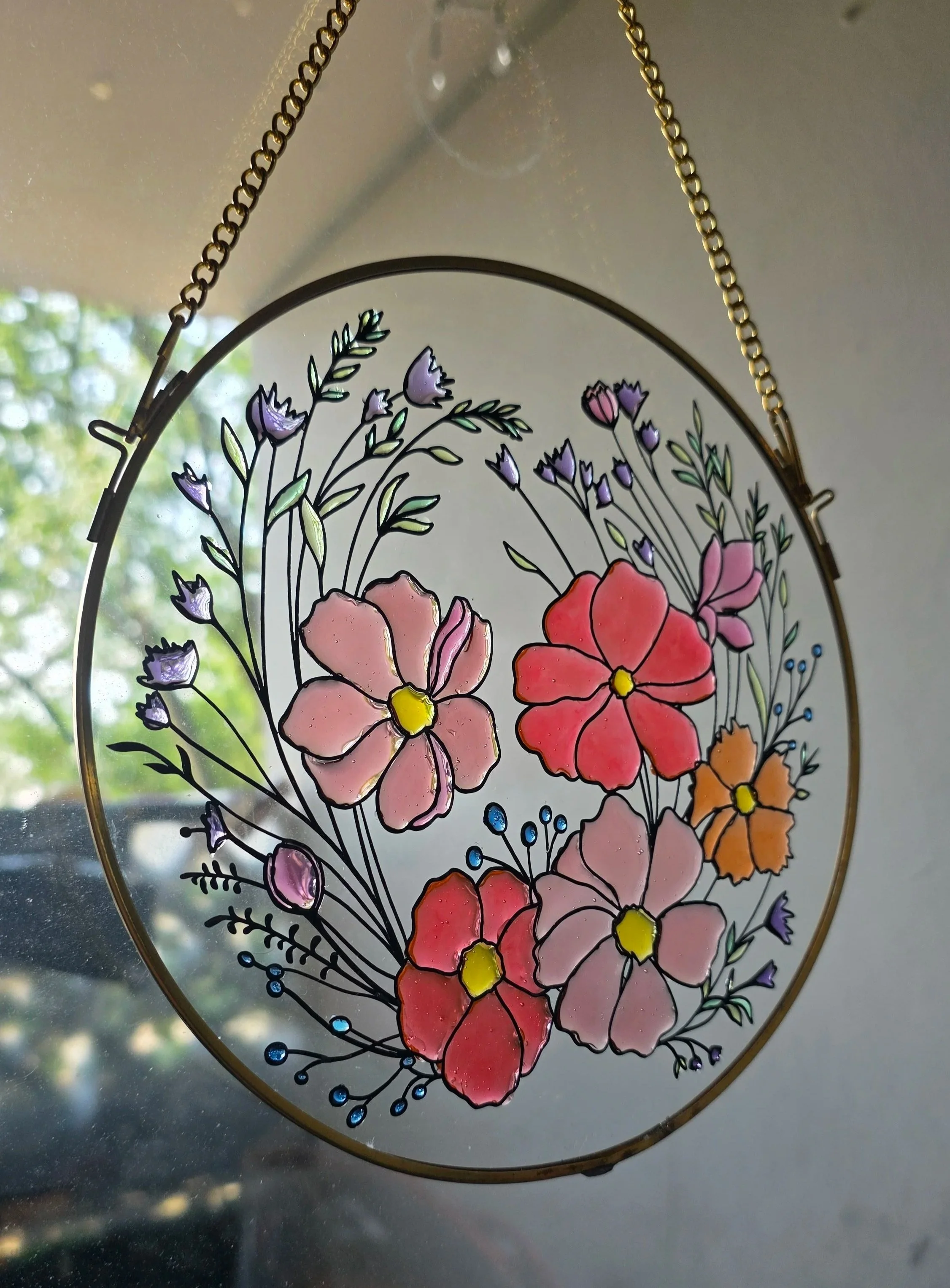 Colorful floral stained glass art hanging with a chain, featuring pink, purple, orange, and yellow flowers and green leaves.