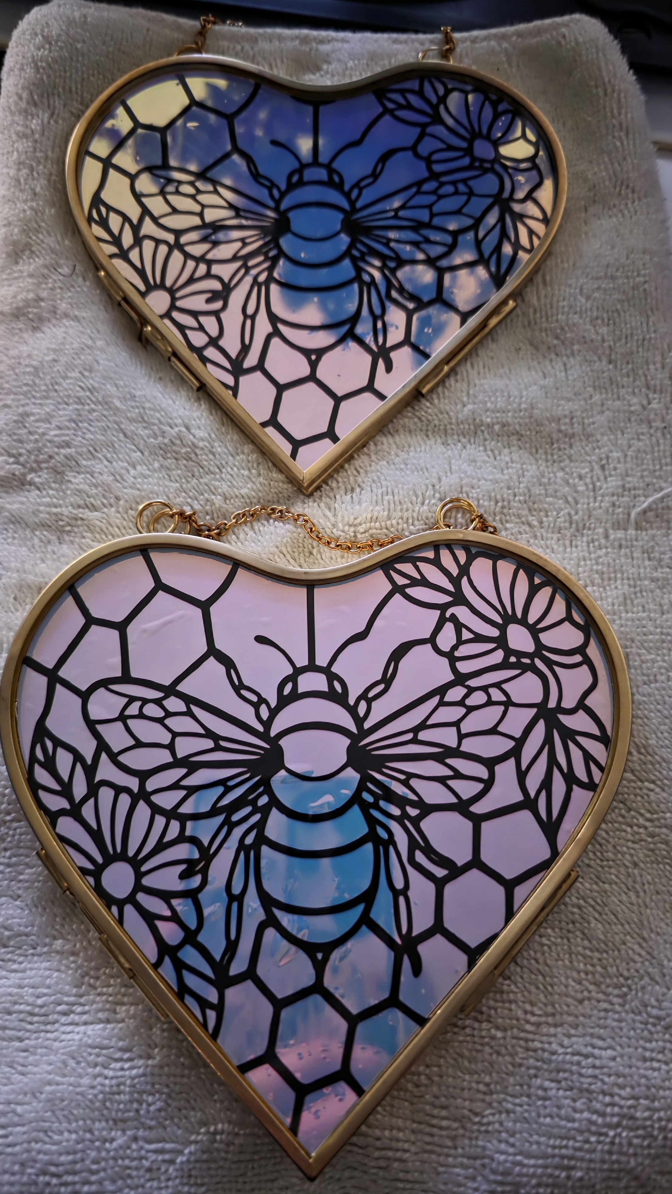 Two heart-shaped stained glass mirrors with bee and honeycomb designs, one placed above the other on a soft surface.