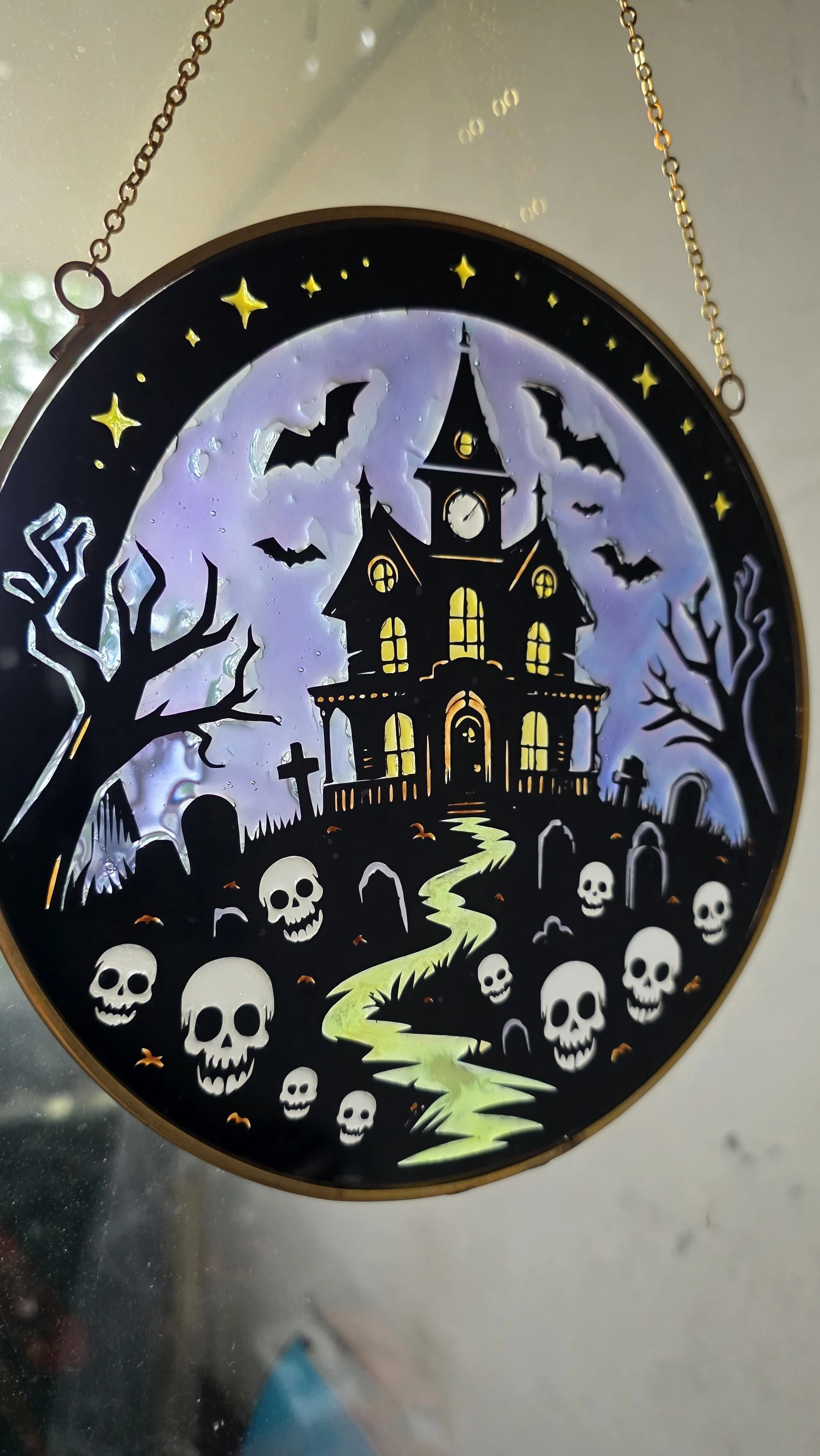 A decorative Halloween-themed clock featuring a haunted house, leafless trees, bats, skulls, a moon, and stars with glow-in-the-dark elements.