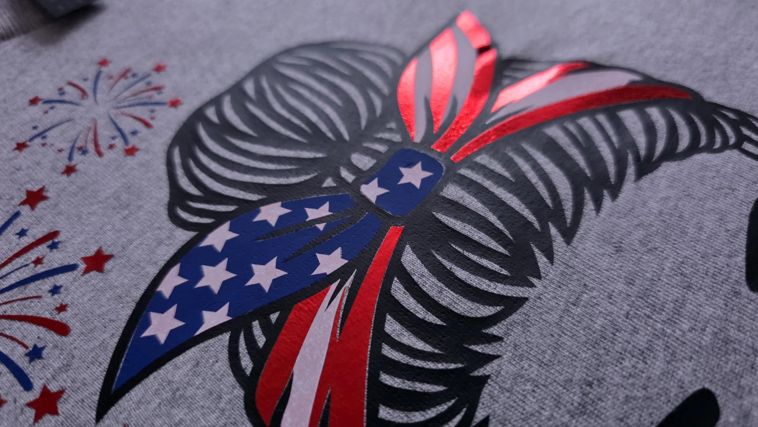 Close-up of a butterfly-shaped sticker or decal with a patriotic American flag theme, featuring red, white, and blue colors, stars, and stripes, on a gray fabric background.