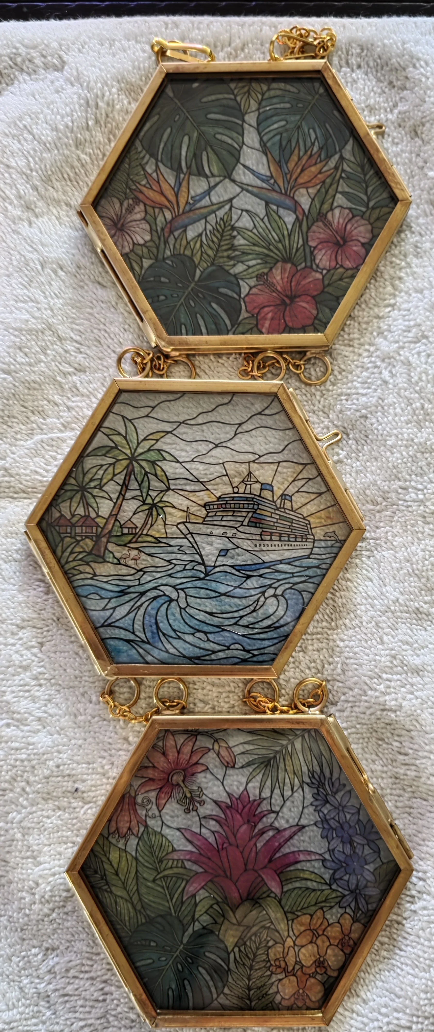 Three hexagonal stained glass trays connected by gold chains, featuring tropical themes. The top tray shows lush green leaves and pink and orange flowers. The middle tray depicts a cruise ship sailing near a tropical island with palm trees and cabana