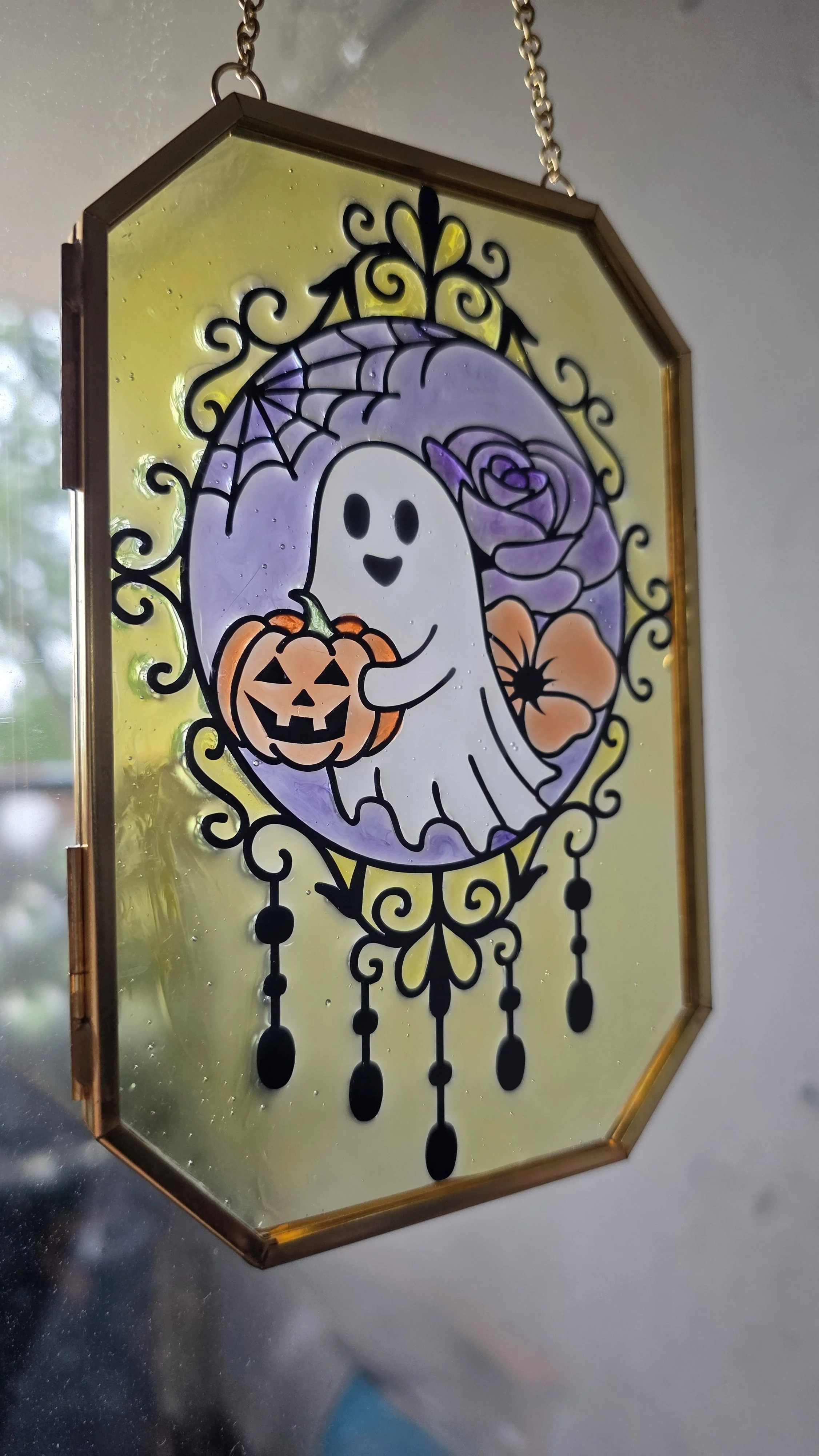 Decorative stained glass Halloween hanging panel featuring a cute ghost holding a jack-o'-lantern, purple flowers, and swirling black accents.