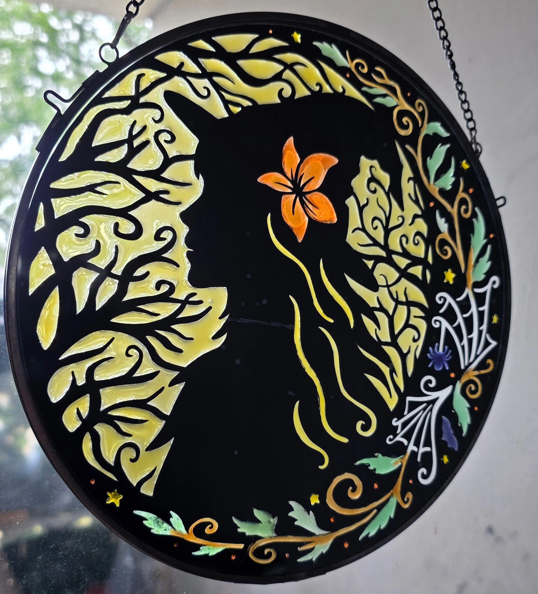 Decorative stained glass art emphasizing a silhouette profile of a woman with an elaborate hairstyle, surrounding swirling floral patterns, leaves, stars, and a butterfly, with a dark background.
