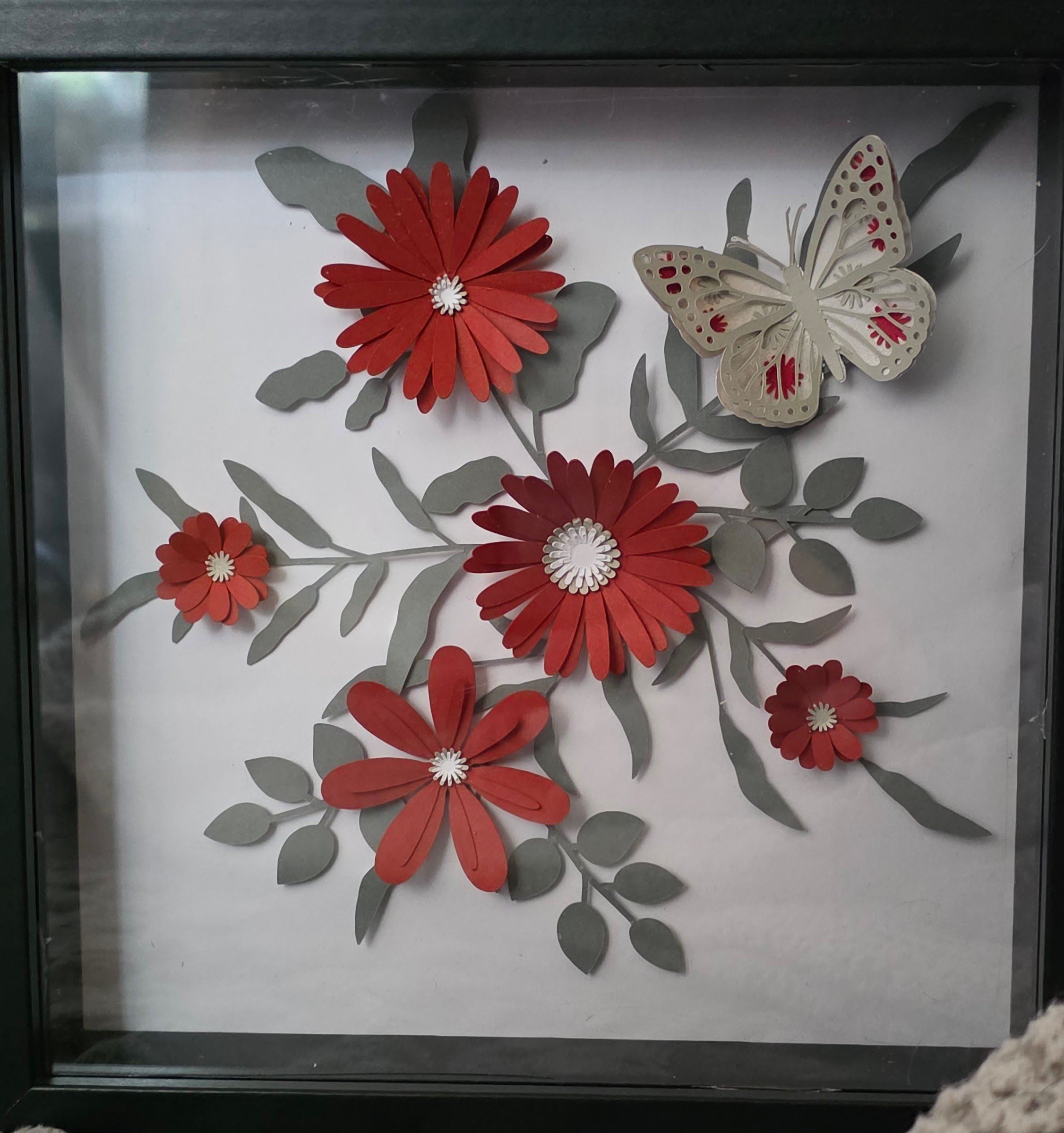 Decorative wall art featuring red paper flowers, grey leaves, and a large cream-colored butterfly with red and pink accents.