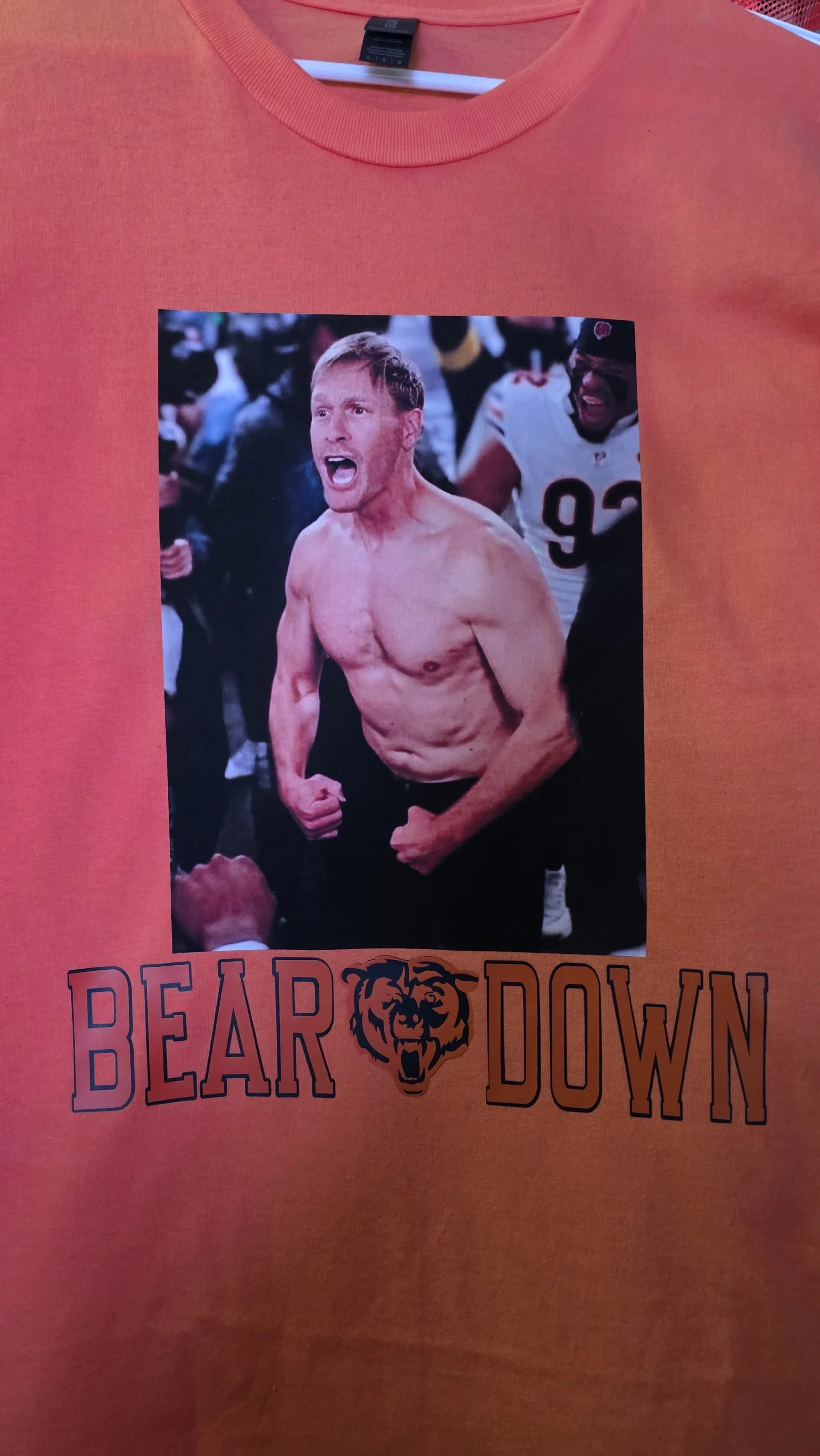 Orange T-shirt with a printed photo of a shirtless man yelling and clenching his fists, in front of a crowd. The text 'BEAR DOWN' with a bear's face in between the words is beneath the photo.