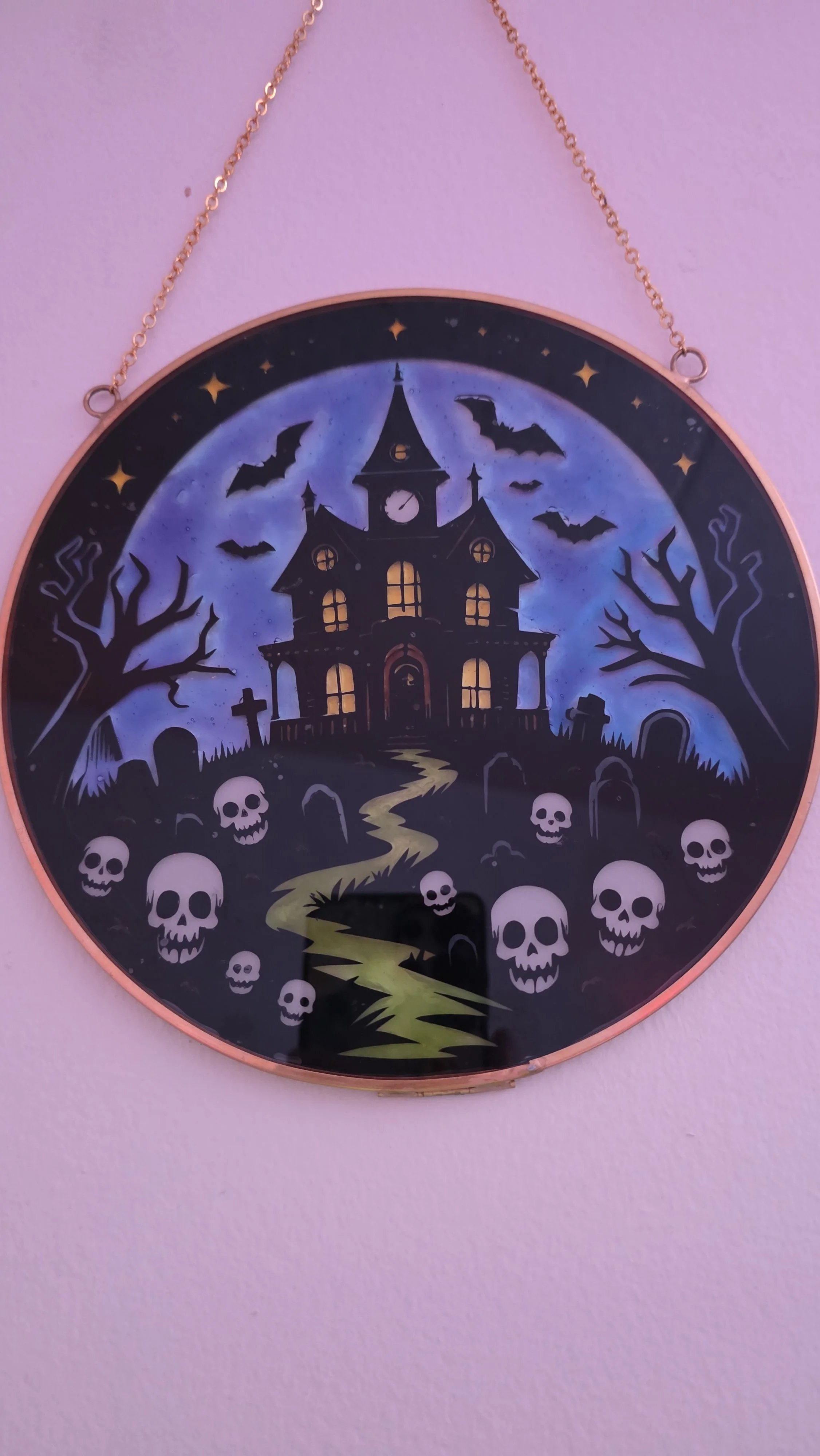 A spooky Halloween-themed clock with a haunted house, bats, skulls, leafless trees, and a winding path against a dark night sky.
