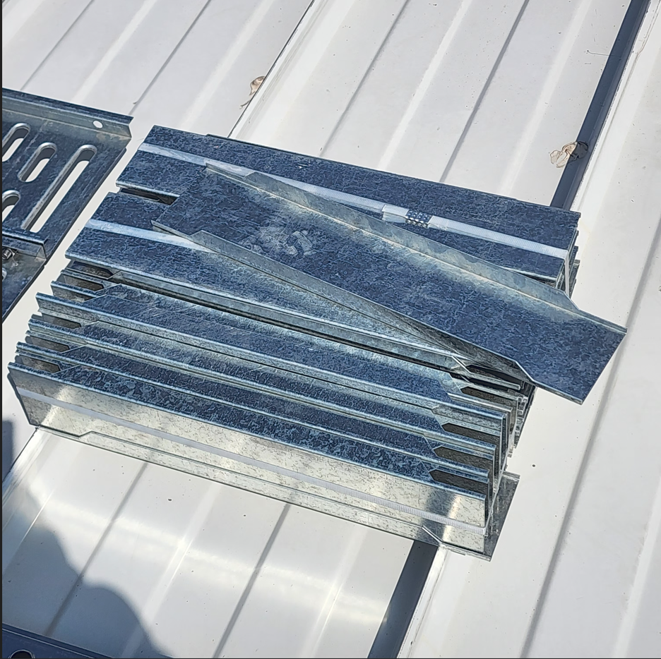 Varios trozos de metal en forma de ángulo con acabado brillante y sin pintar, colocados sobre una superficie metálica blanca.