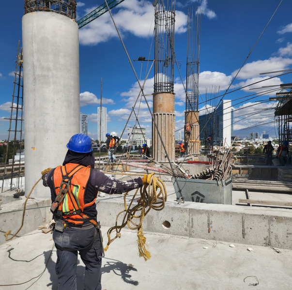 Trabajadores de construcción en un edificio en construcción con estructuras de acero y cubiertas de concreto, en un día soleado.