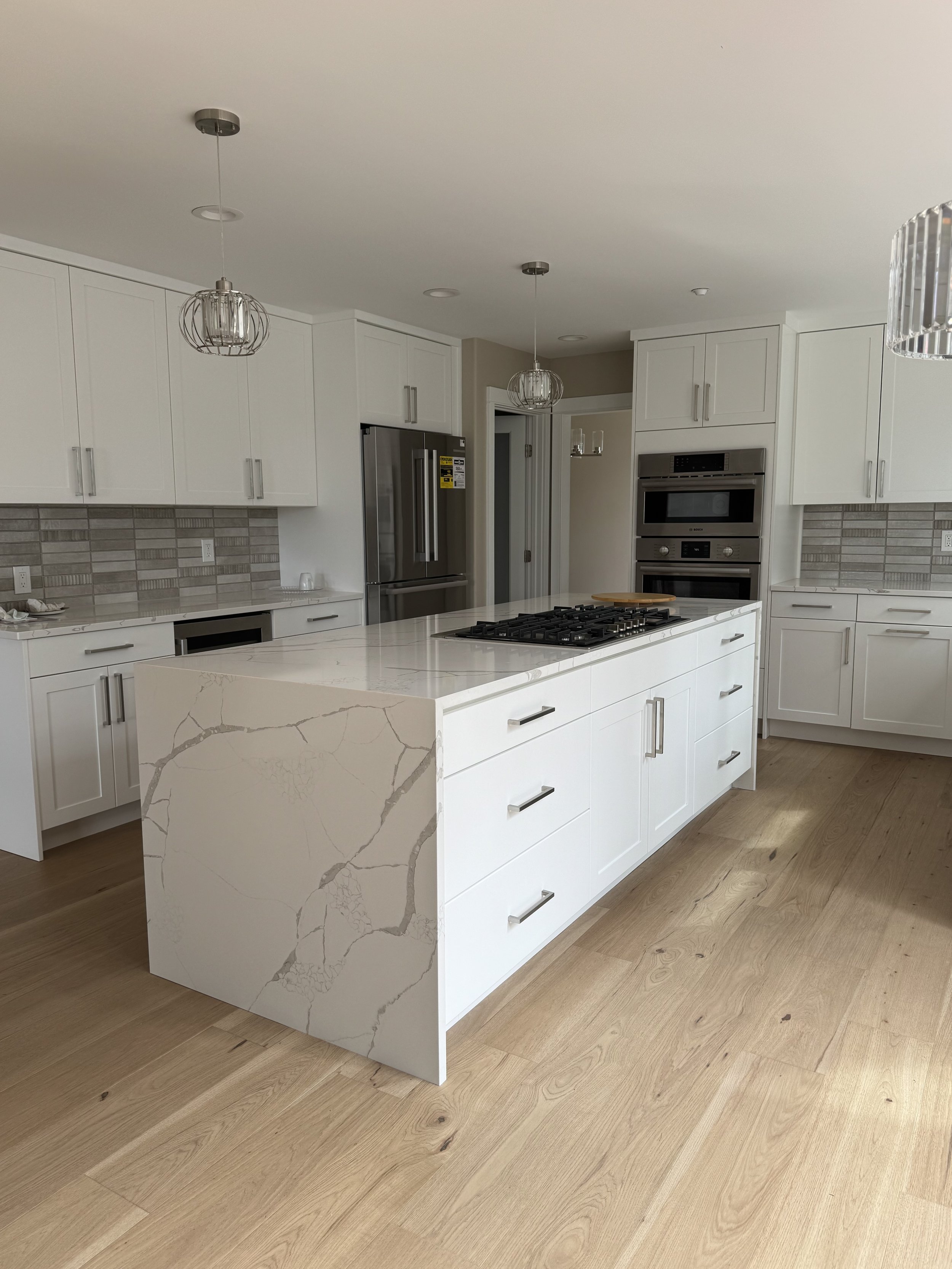 Kitchen renovation in Bellevue/Kirkland/Medina/Seattle area featuring a quartz waterfall island, gas cooktop, and custom white cabinetry by Tennison Design Build.