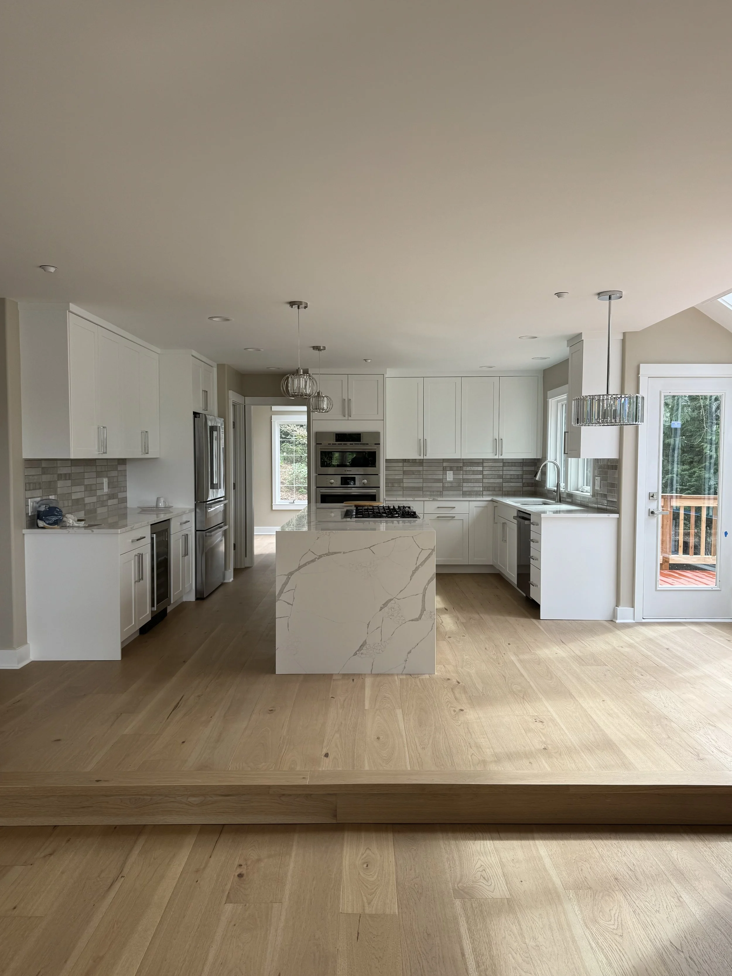 "Custom kitchen remodel by Tennison Design Build featuring white shaker cabinets, a quartz waterfall island, and wide-plank white oak flooring — Seattle area general contractor."
