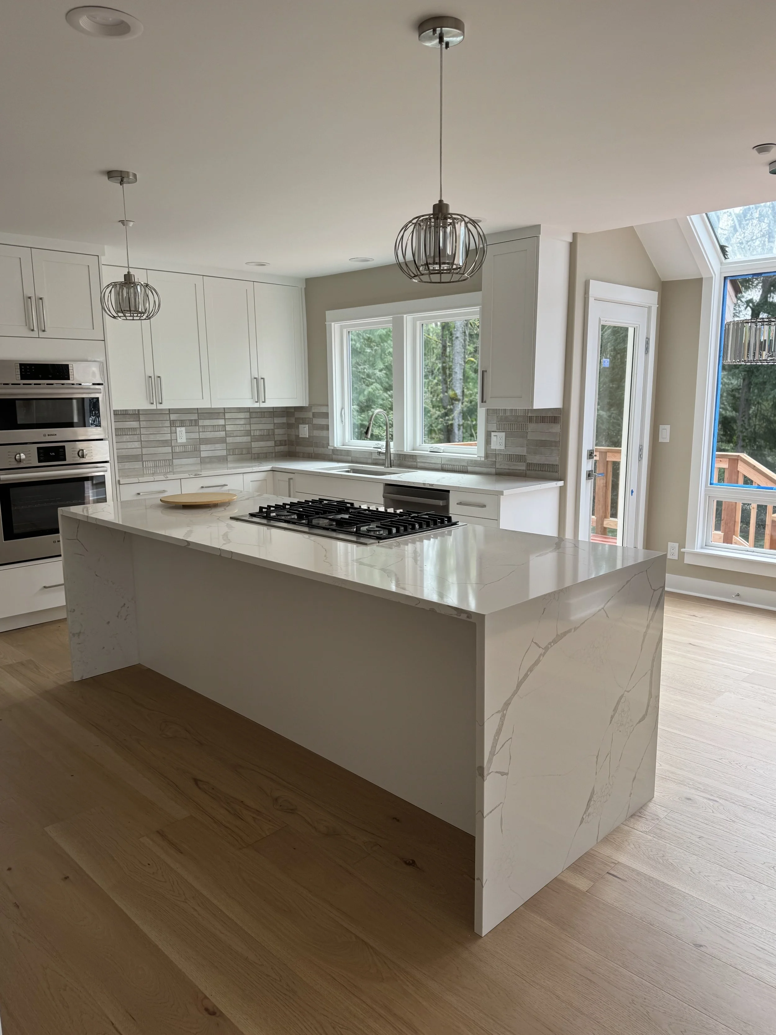 Custom kitchen remodel by Tennison Design Build with a quartz waterfall island, built-in gas cooktop, white cabinetry, and wide-plank oak flooring — Seattle area design-build luxury contractor.