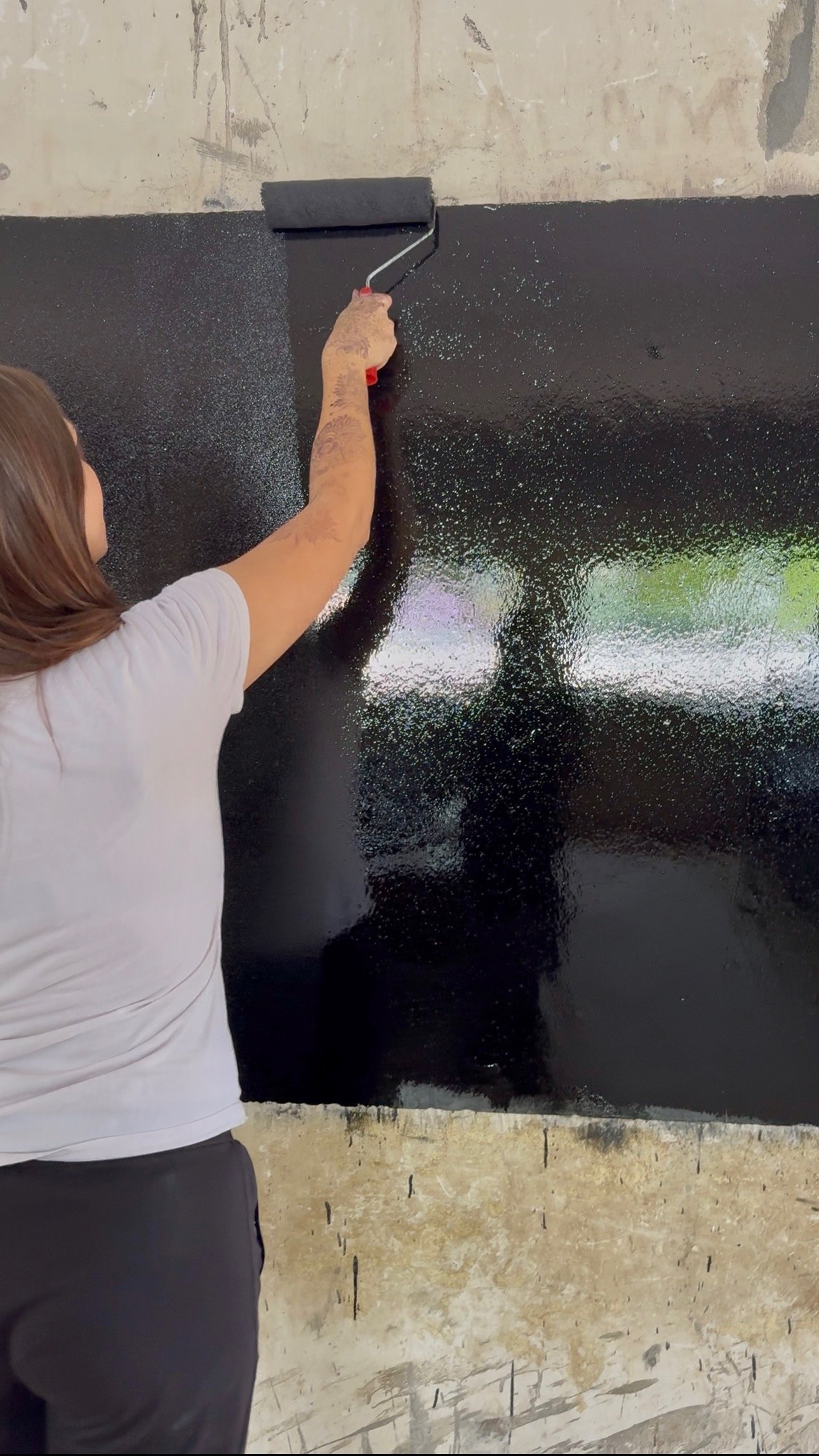 A person is painting a black wall with a roller brush.
