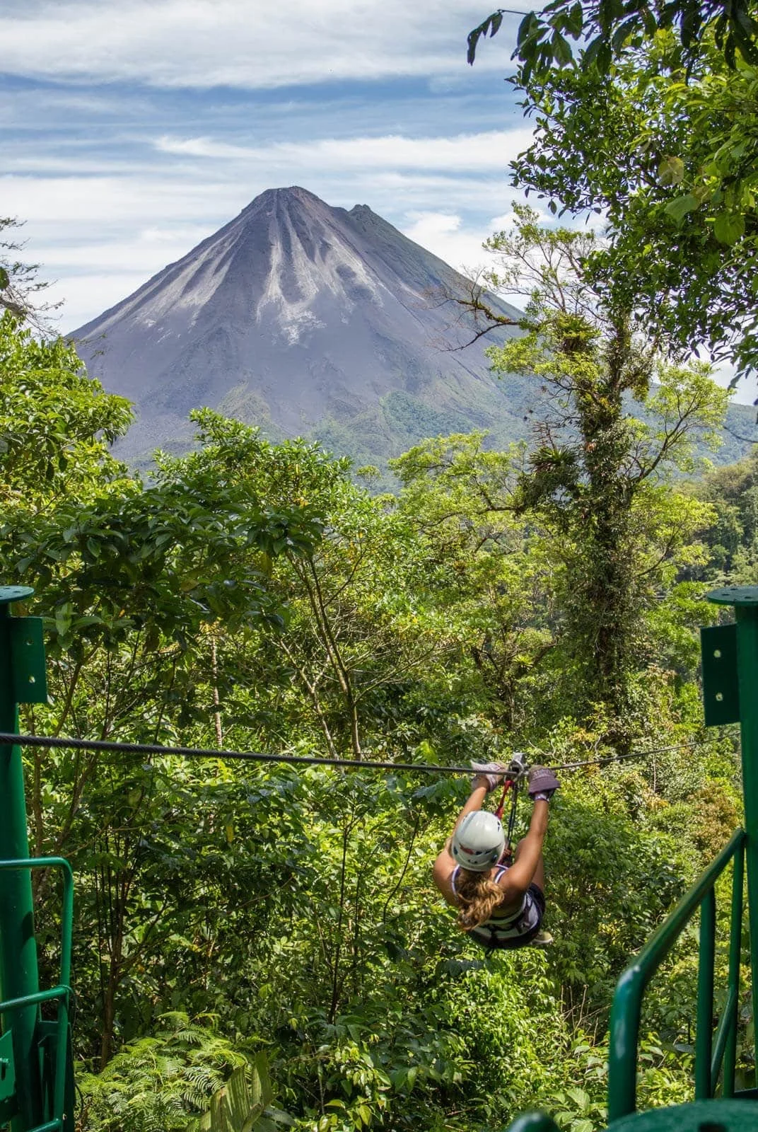 A person ziplining through a lush green forest with a volcano in the background.