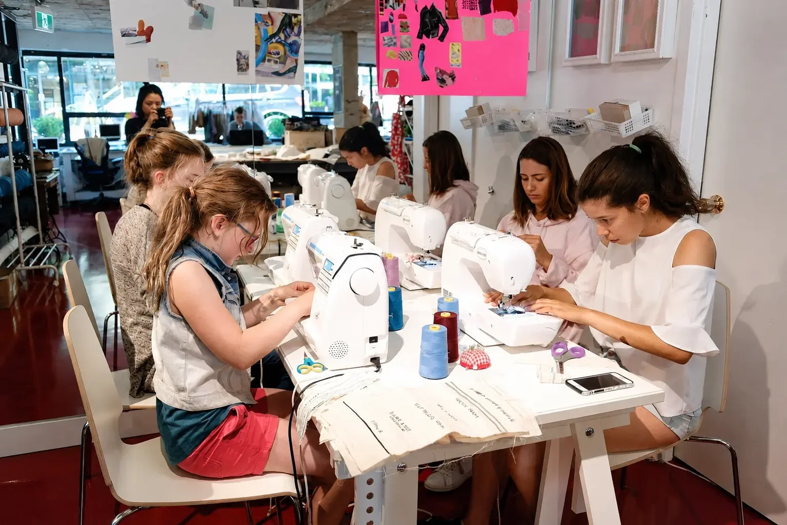 Group of children sewing at a long table in a classroom or workshop.