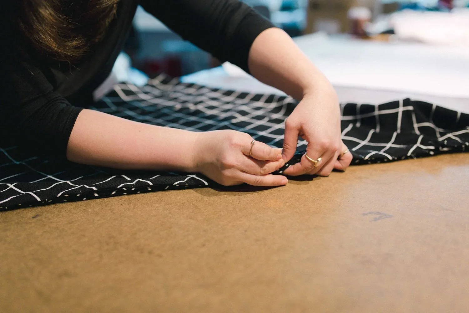 Person sewing black fabric with white grid pattern on a brown work surface.