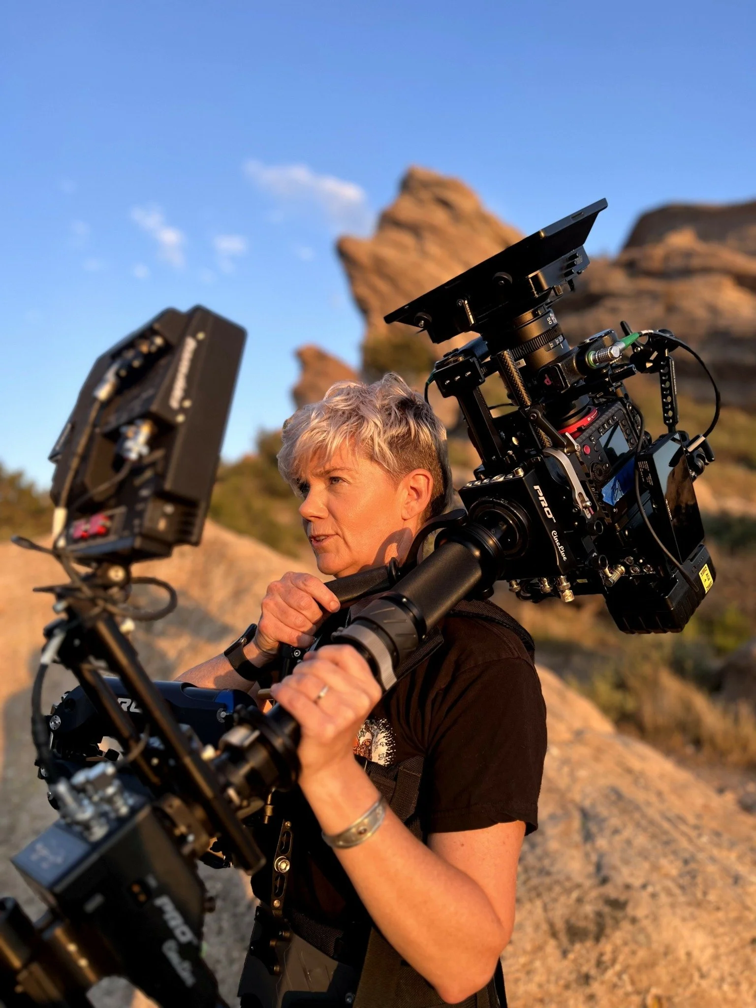 Person operating professional camera equipment outdoors with rocky landscape and clear sky in the background.