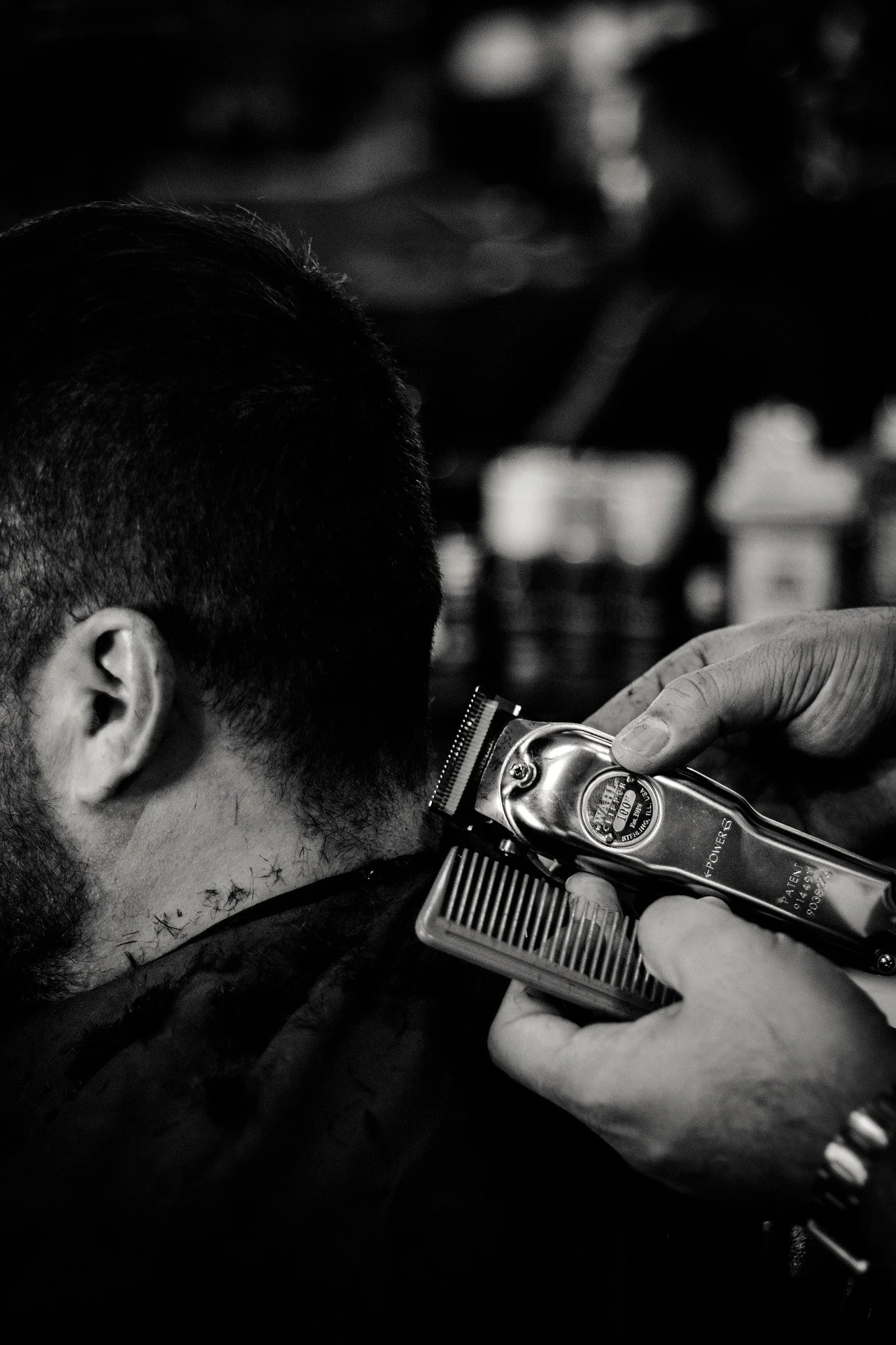 A person getting a haircut at a barbershop with a handheld electric clipper, focusing on the side of their head and neck area.