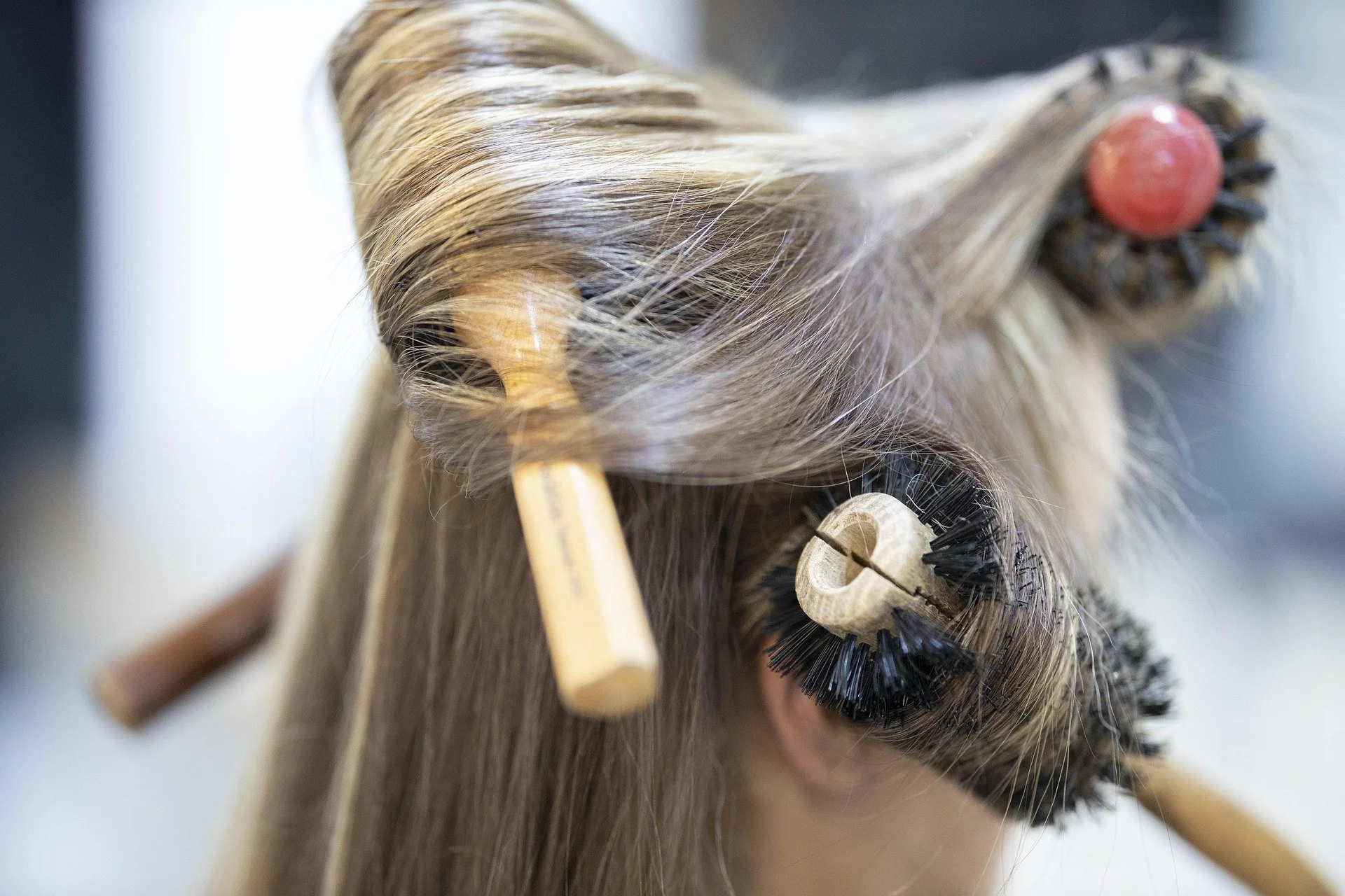 A close-up of a person's hair being styled with rollers and curlers, with wooden sticks used in the hair styling process.