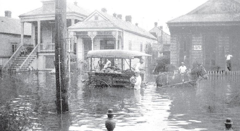 Flooded street with several people including some on a wagon pulled by a horse and others wading through water, in front of houses.