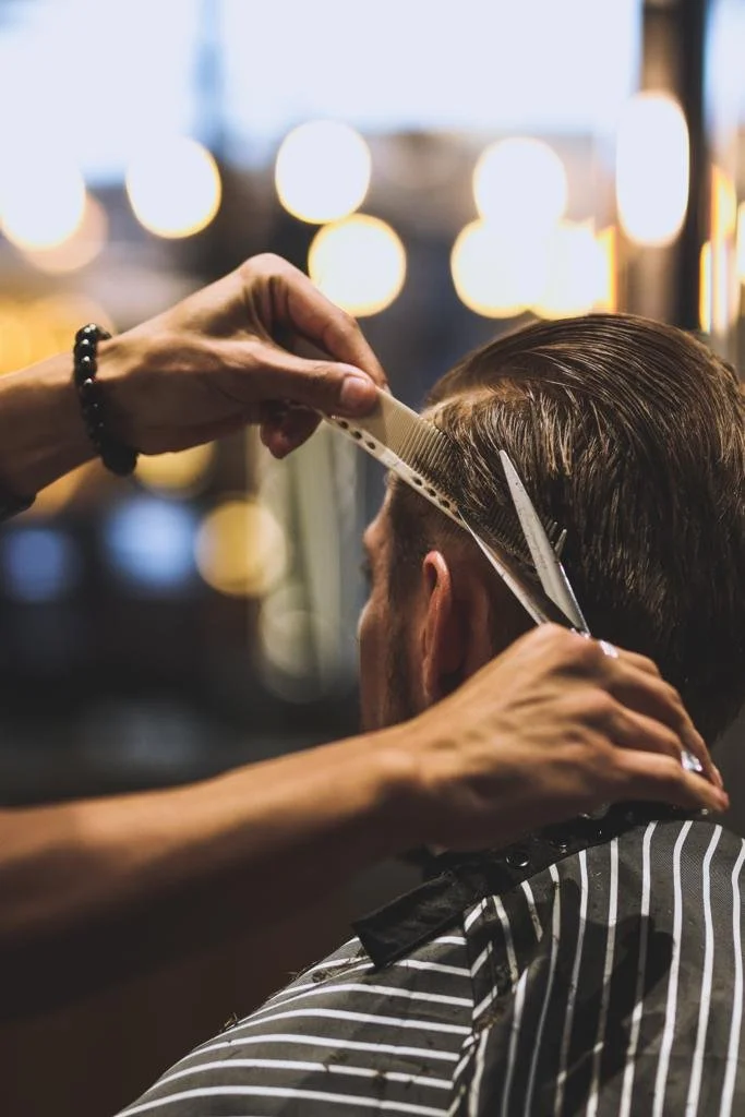 Barber trimming a man's hair with scissors and a comb in a salon