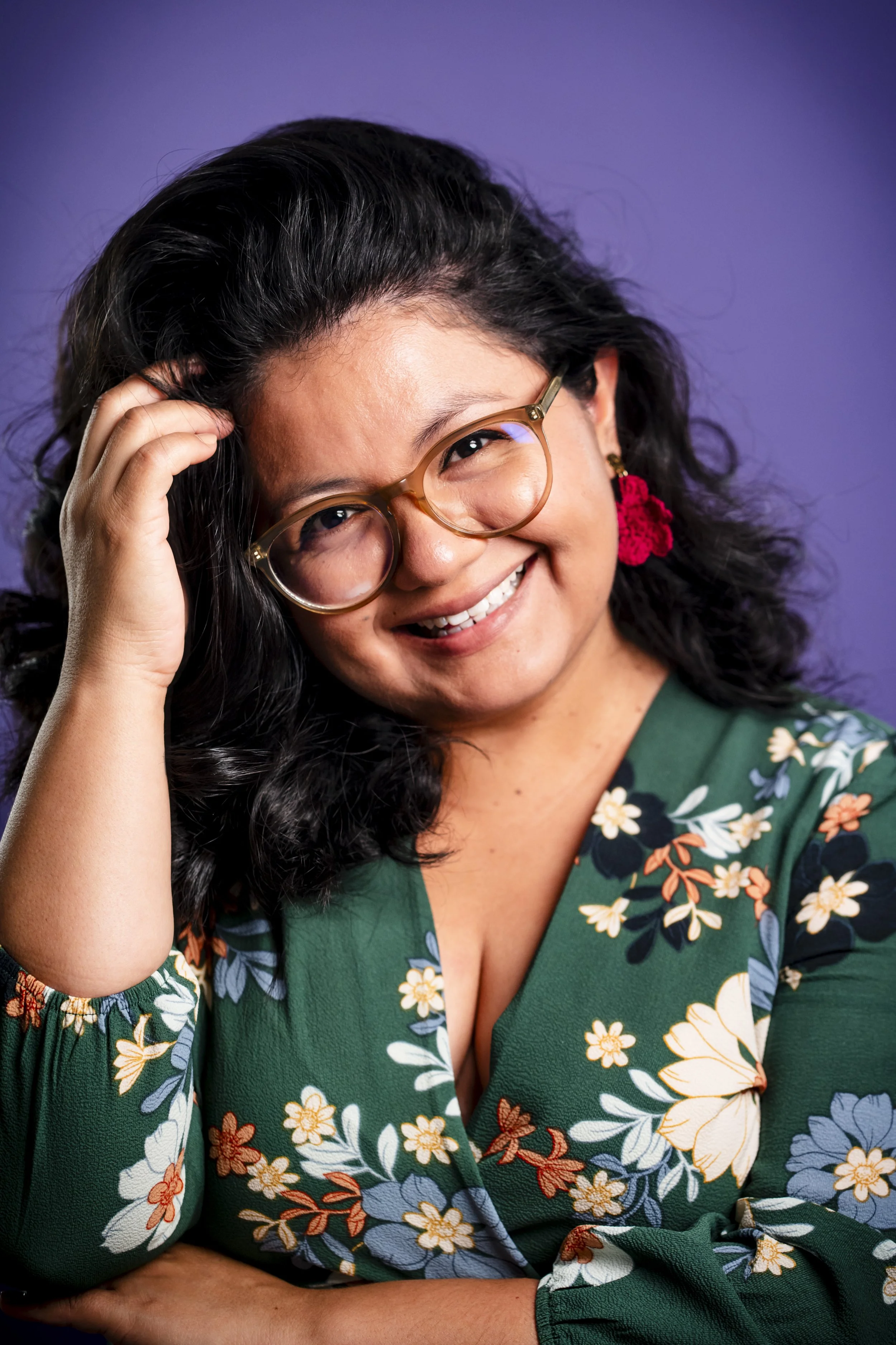 Portrait of Tania Pilz. She is a young adult with brown skin and dark, curly hair, wearing a green floral dress and smiling at the camera.