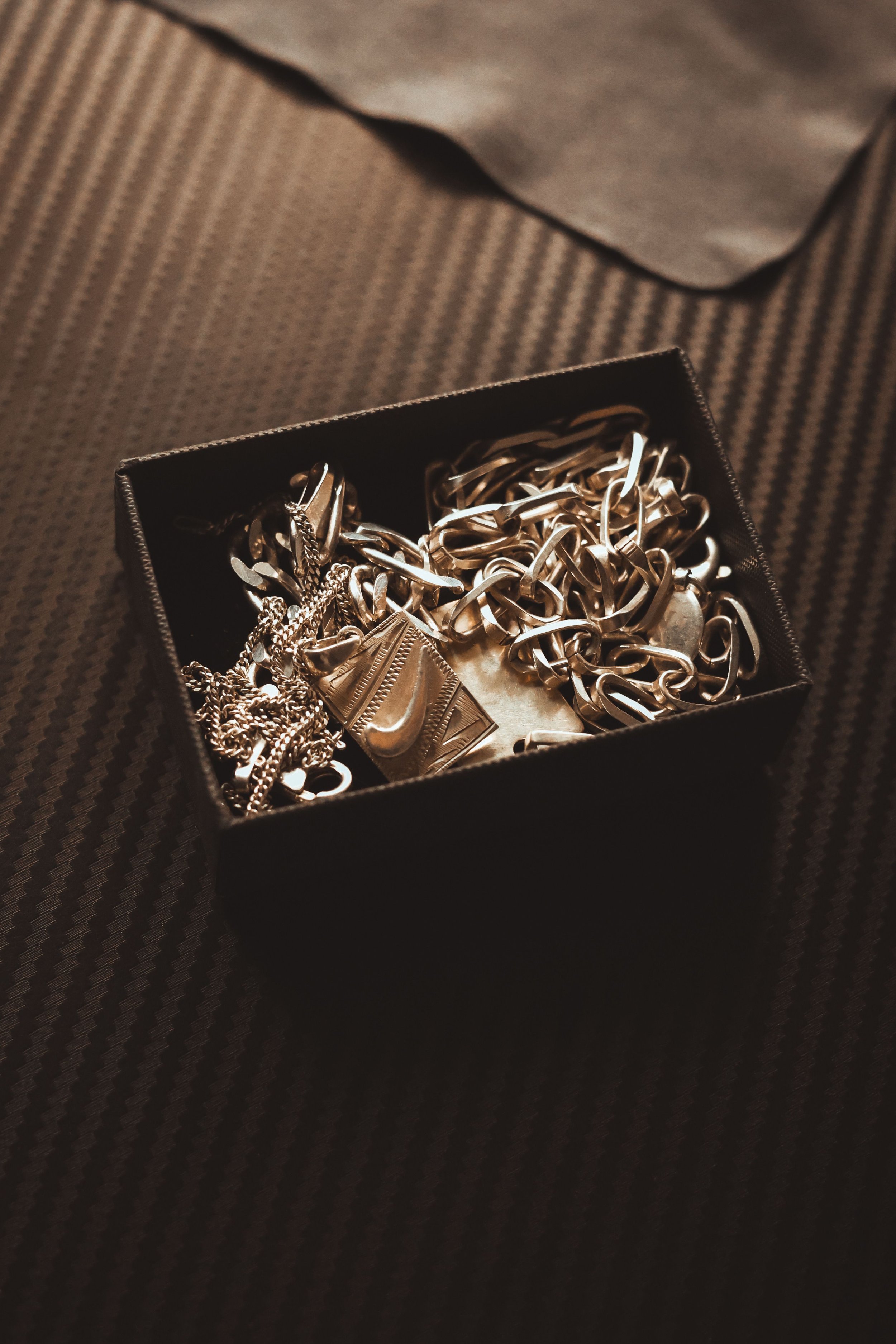 Une boîte contenant des colliers, des bracelets et des pendentifs en métal argenté, posée sur un tissu à motifs.