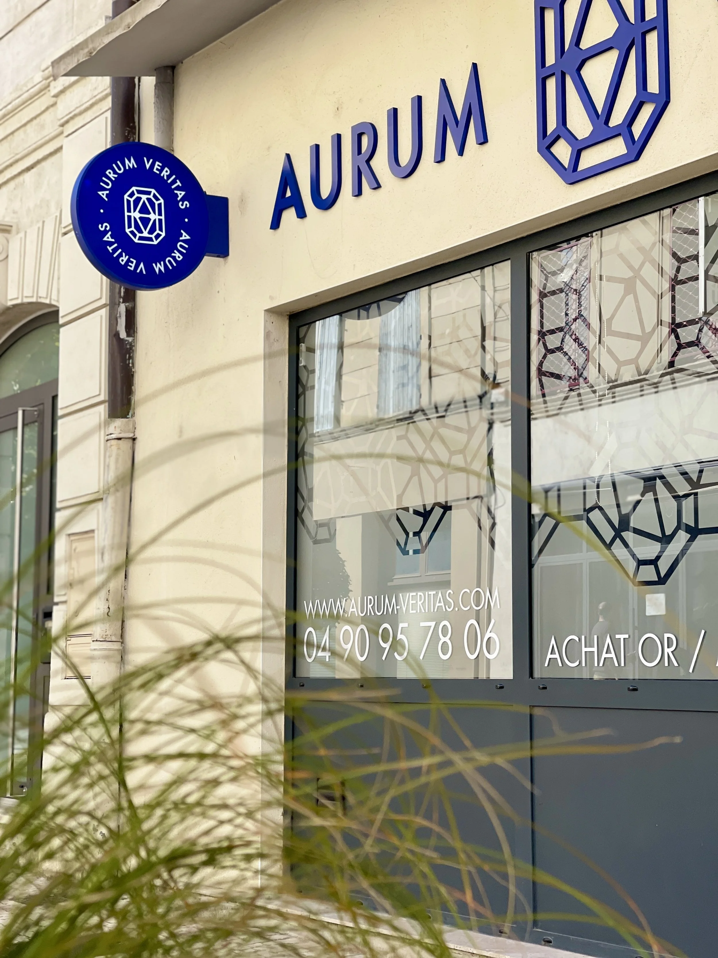 Vitrine d'une boutique avec le nom 'Aurum' en lettres bleues et un logo en forme de diamant bleu. Site internet www.aurum-veritas.com et numéro de téléphone affichés.