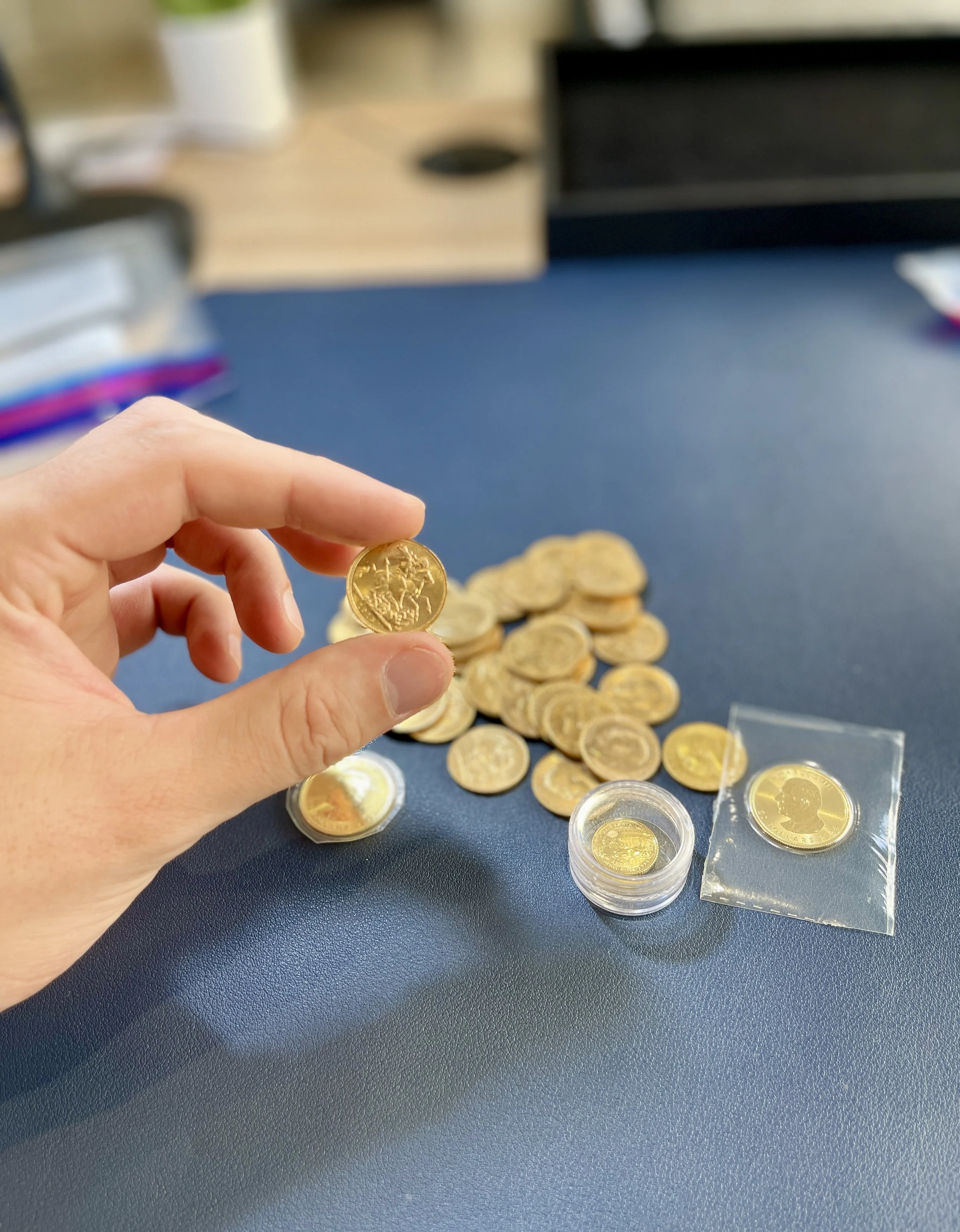 Main d'une personne tenant une pièce de monnaie en or, avec plusieurs autres pièces de monnaie en or sur une table. Fundo flou dans un environnement intérieur.