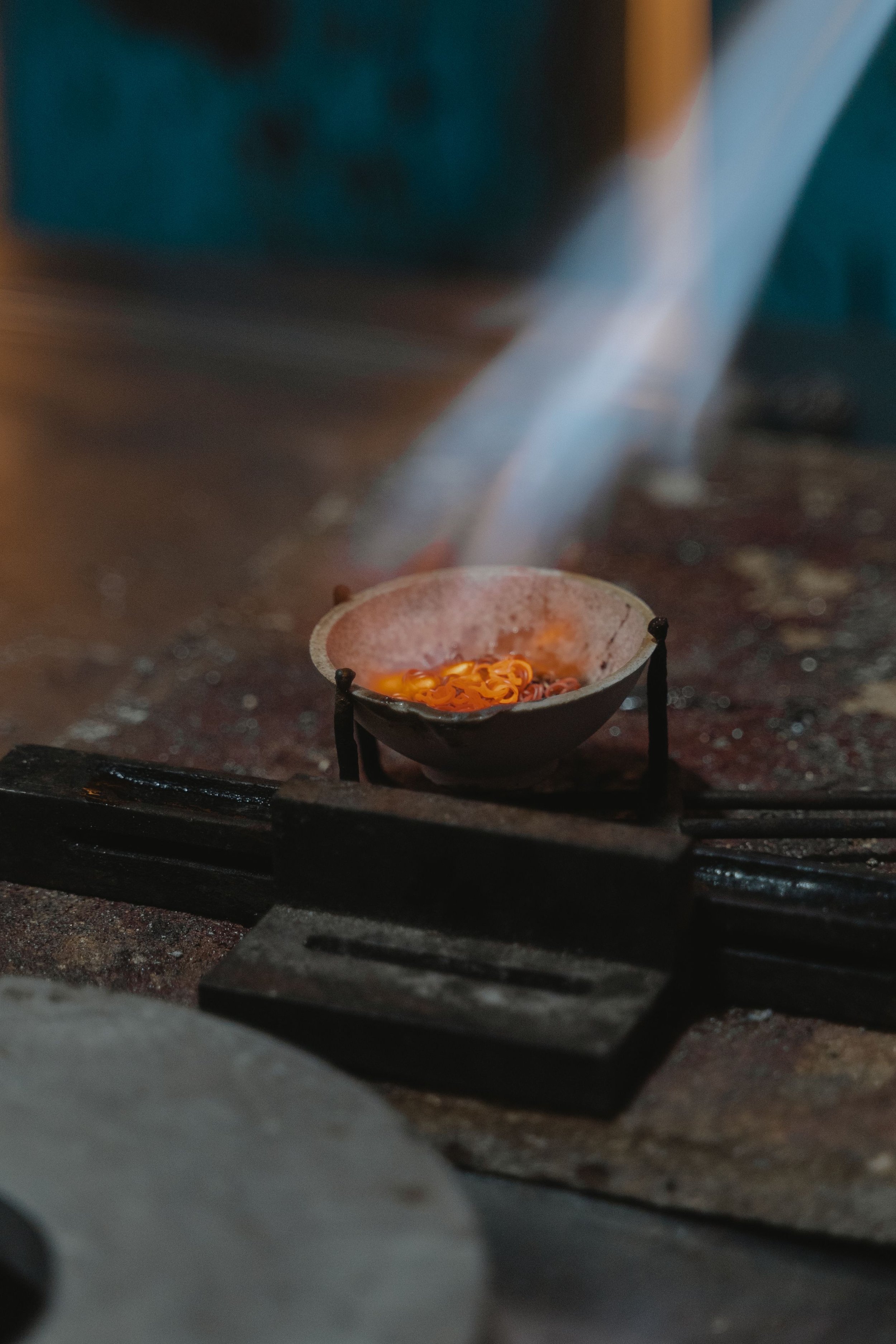 Une petite coupe en métal contenant des bougies allumées, placée sur une surface en bois, avec une flamme visible et de la fumée s'élevant.
