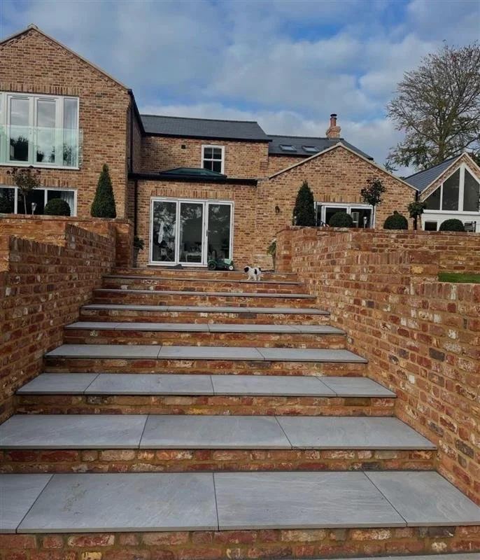Brick staircase leading to backyard of a brick house with sliding glass doors, lawn, and trees