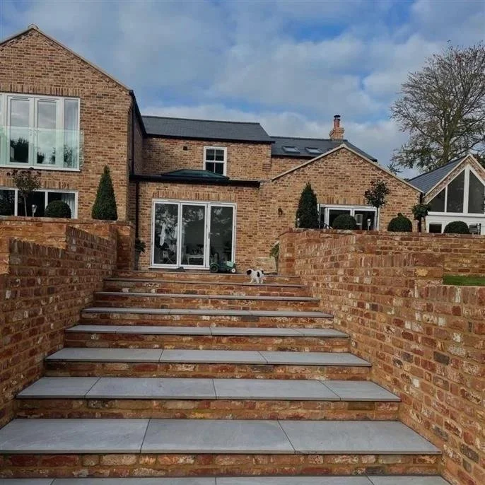Brick house with large sliding glass doors, stairs made of bricks and tiles, and landscaped bushes and trees in the yard.