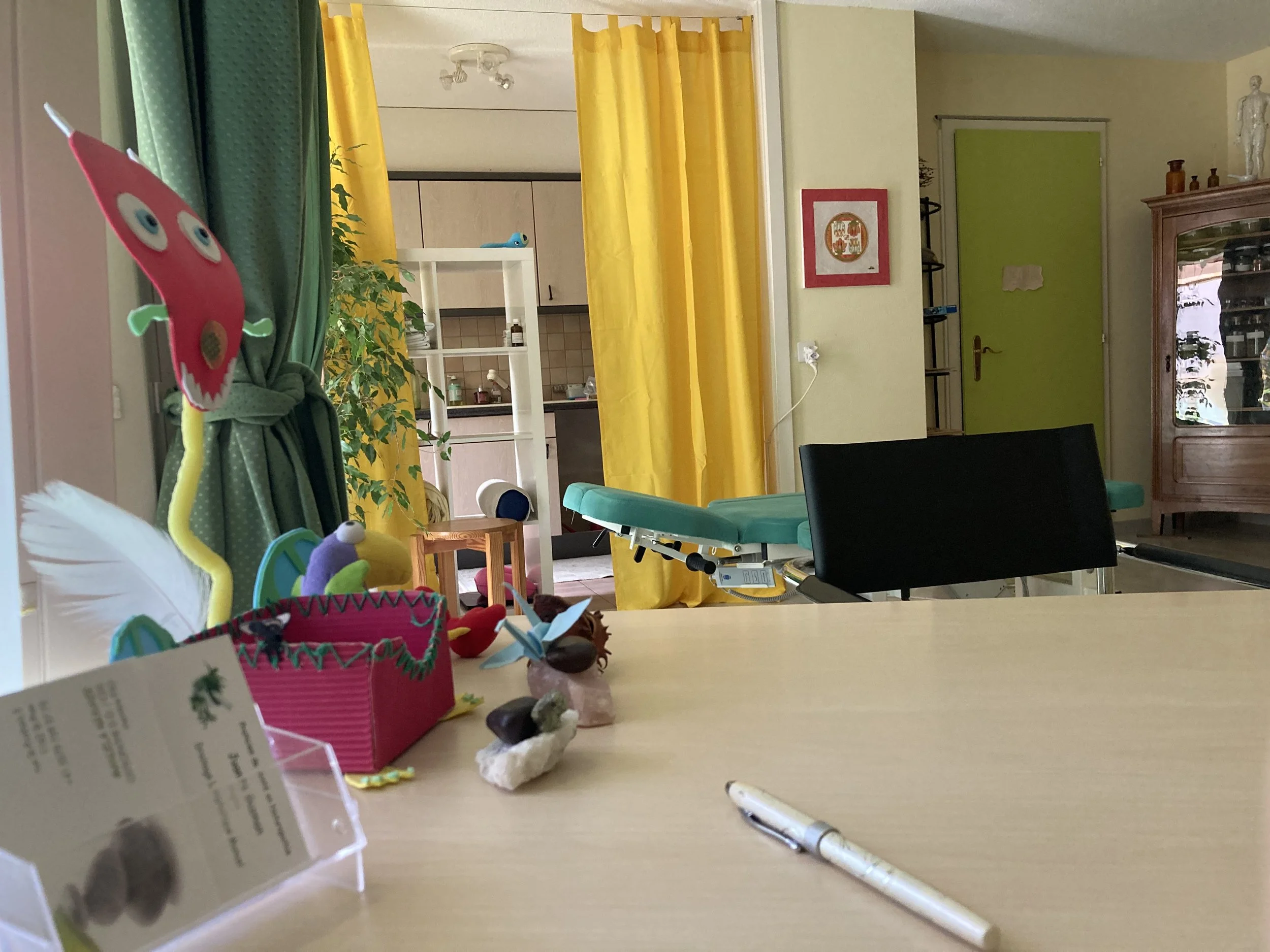 Une table avec des petits objets décoratifs, une plume, et un morceau de papier. En arrière-plan, des rideaux jaunes et une pièce avec des meubles et des décorations.